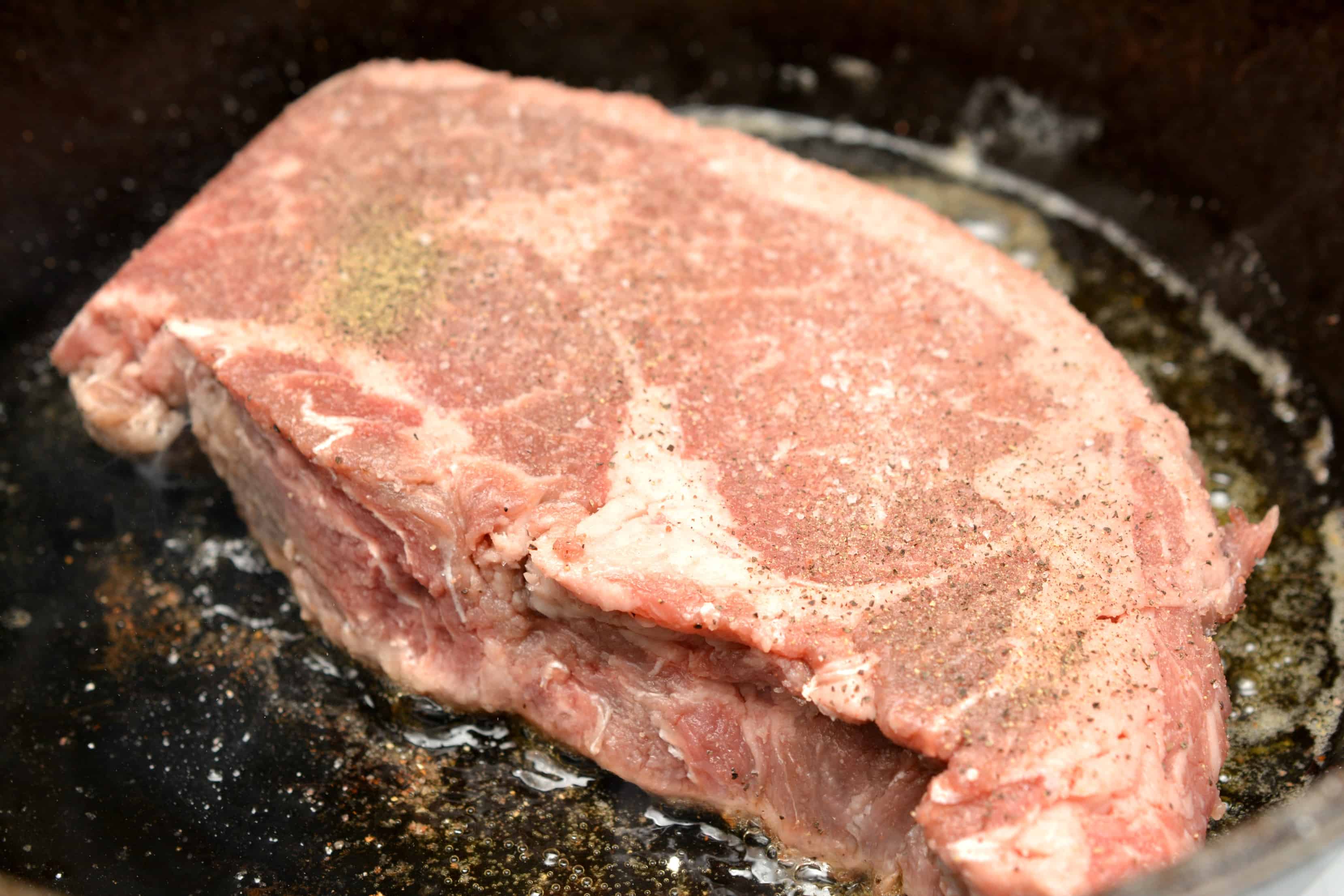 seasoned raw steak in cast iron skillet