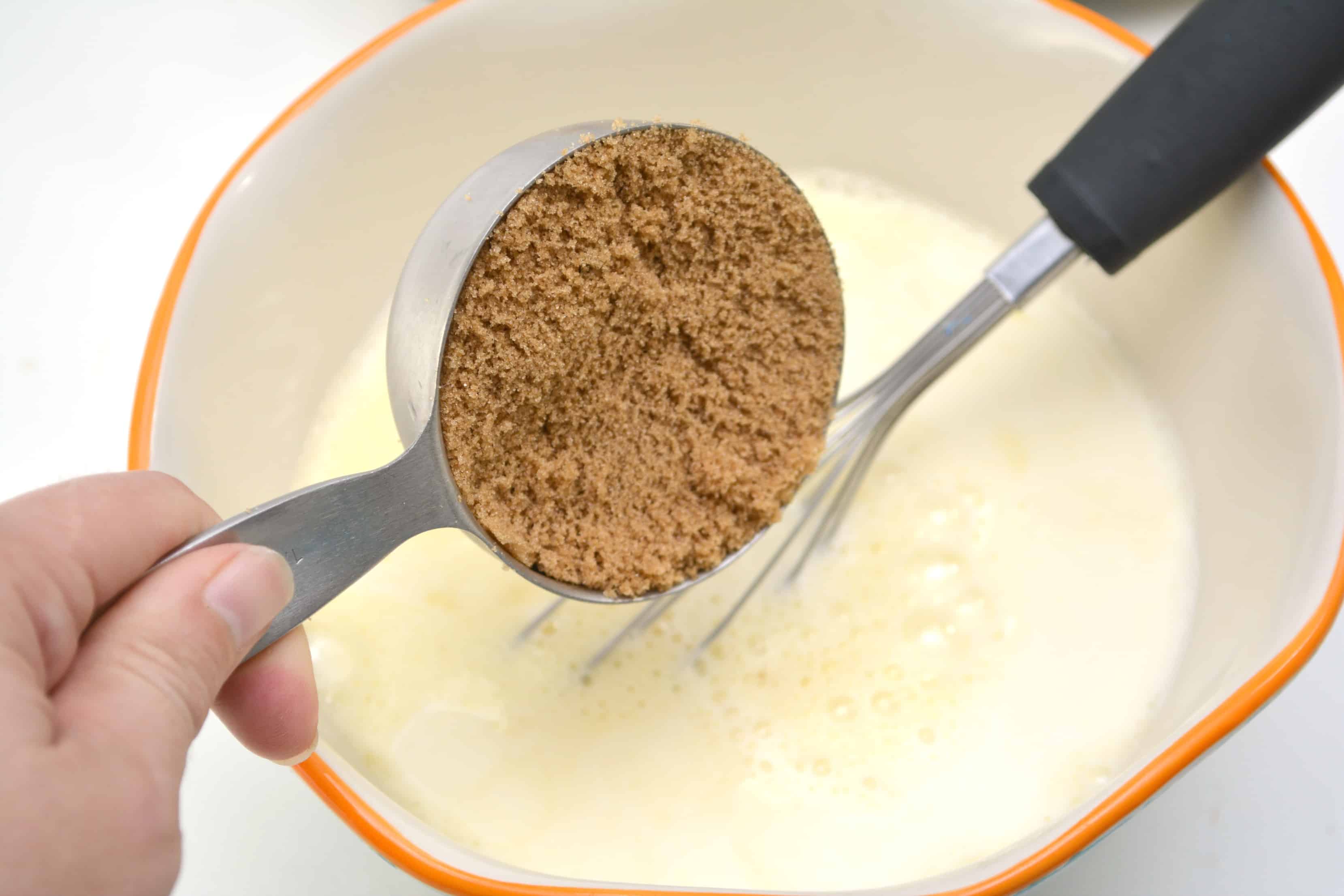 adding brown sugar to the egg mixture in a white bowl