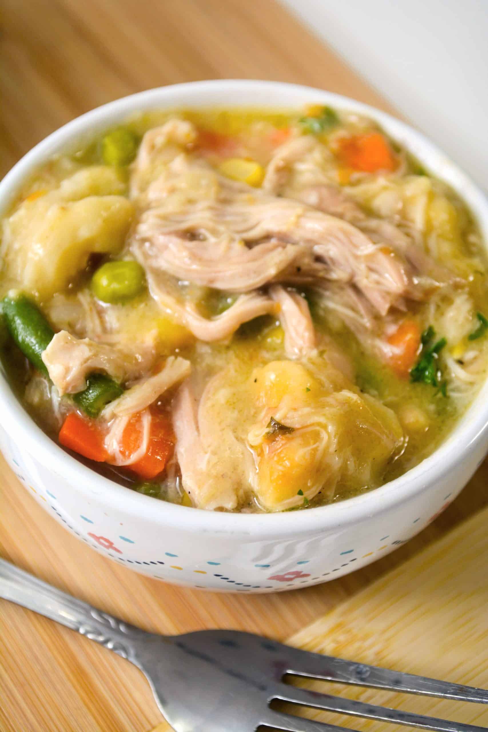 bowl of chicken and dumplings on wood cutting board