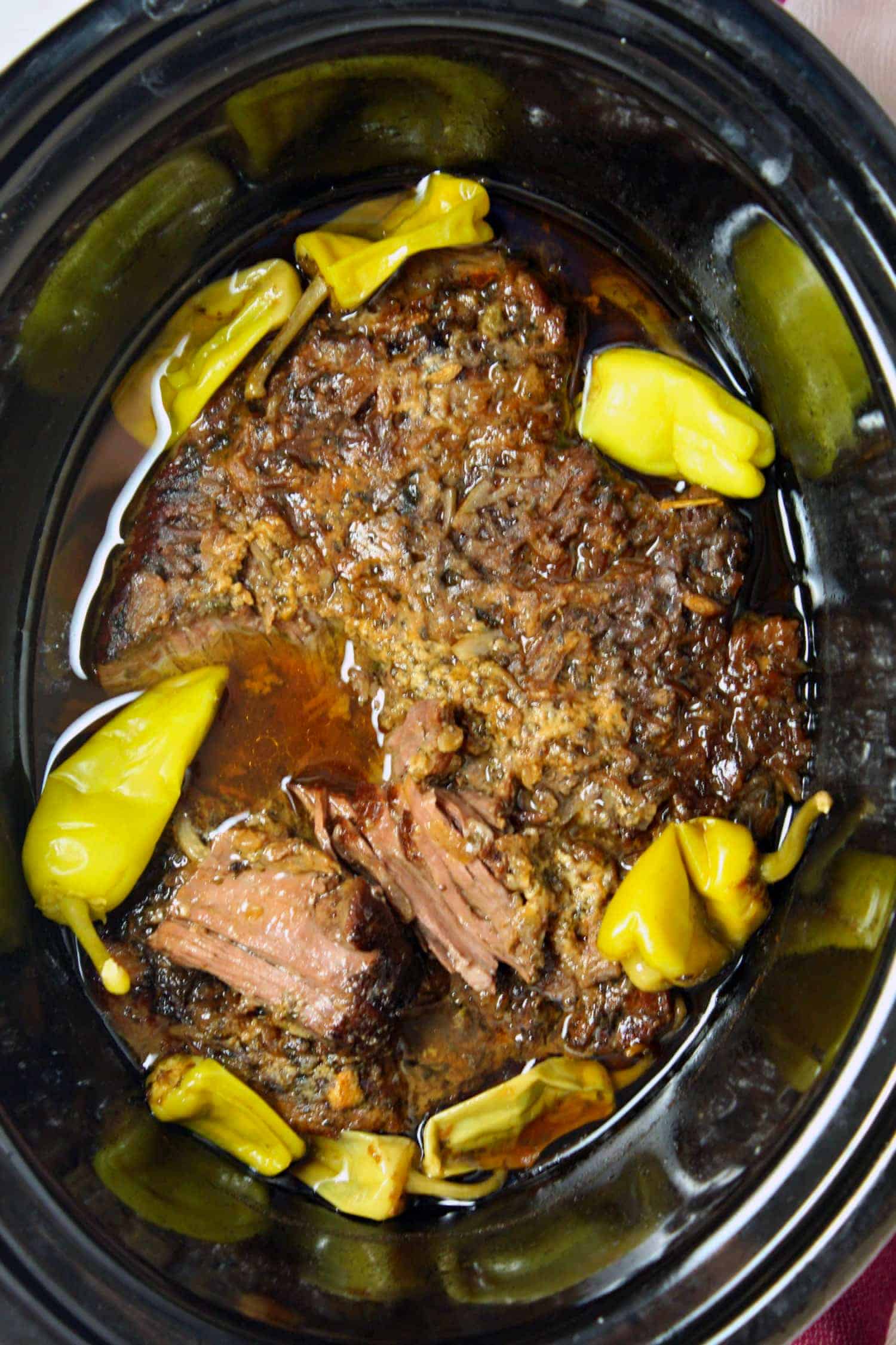 pot roast in slow cooker with peppers around it
