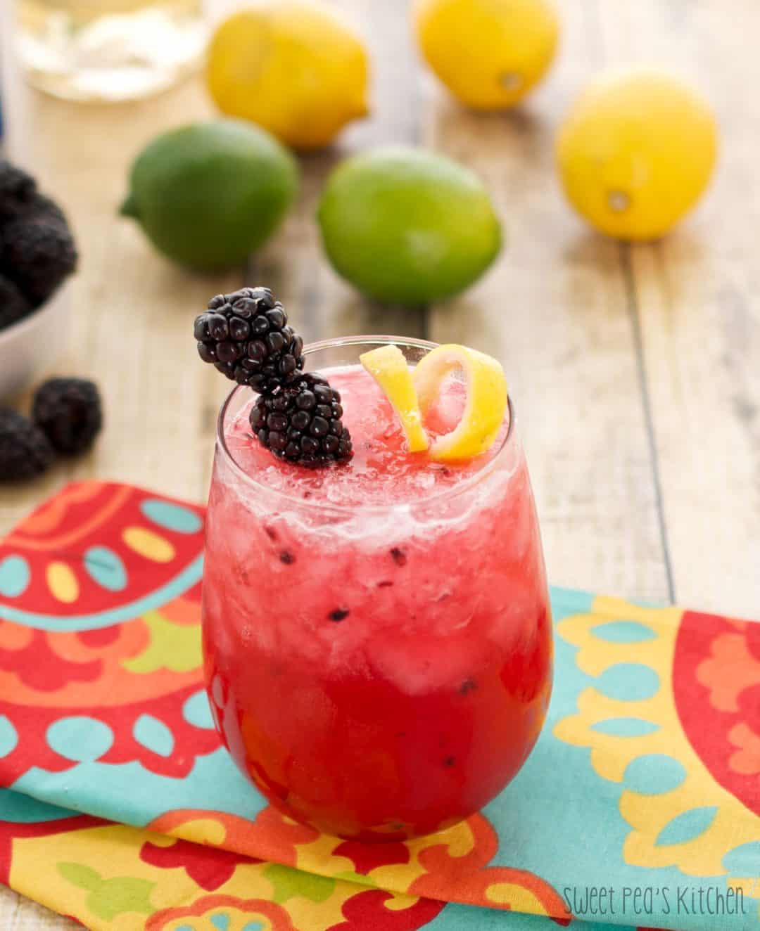 A small glass of blackberry bramble sitting on a colorful napkin on a wooden surface