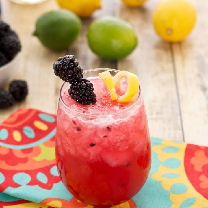 A small glass of blackberry bramble sitting on a colorful napkin on a wooden surface