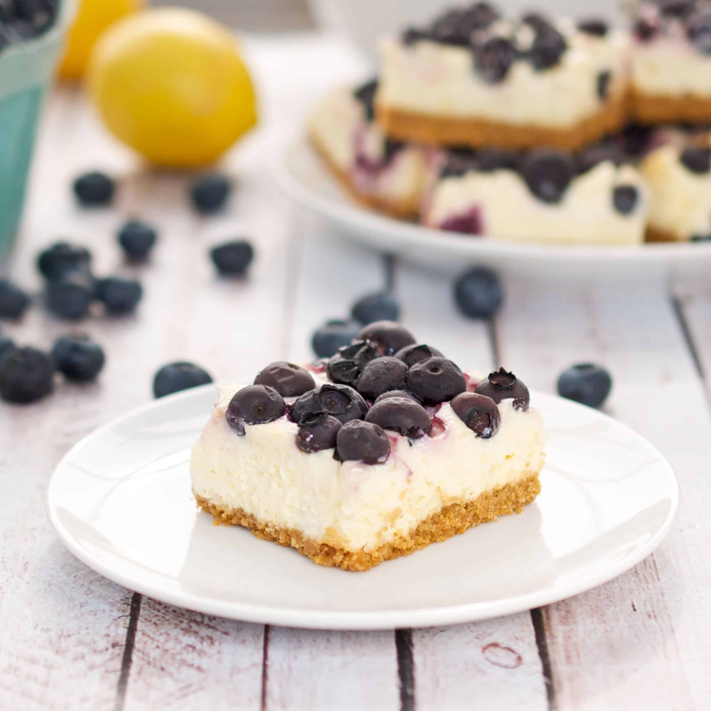 lemon cheesecake bars with bluberries on a white plate