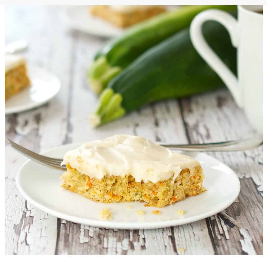 Carrot Zucchini Bars with Cream Cheese Frosting on a white plate with zucchini in the background