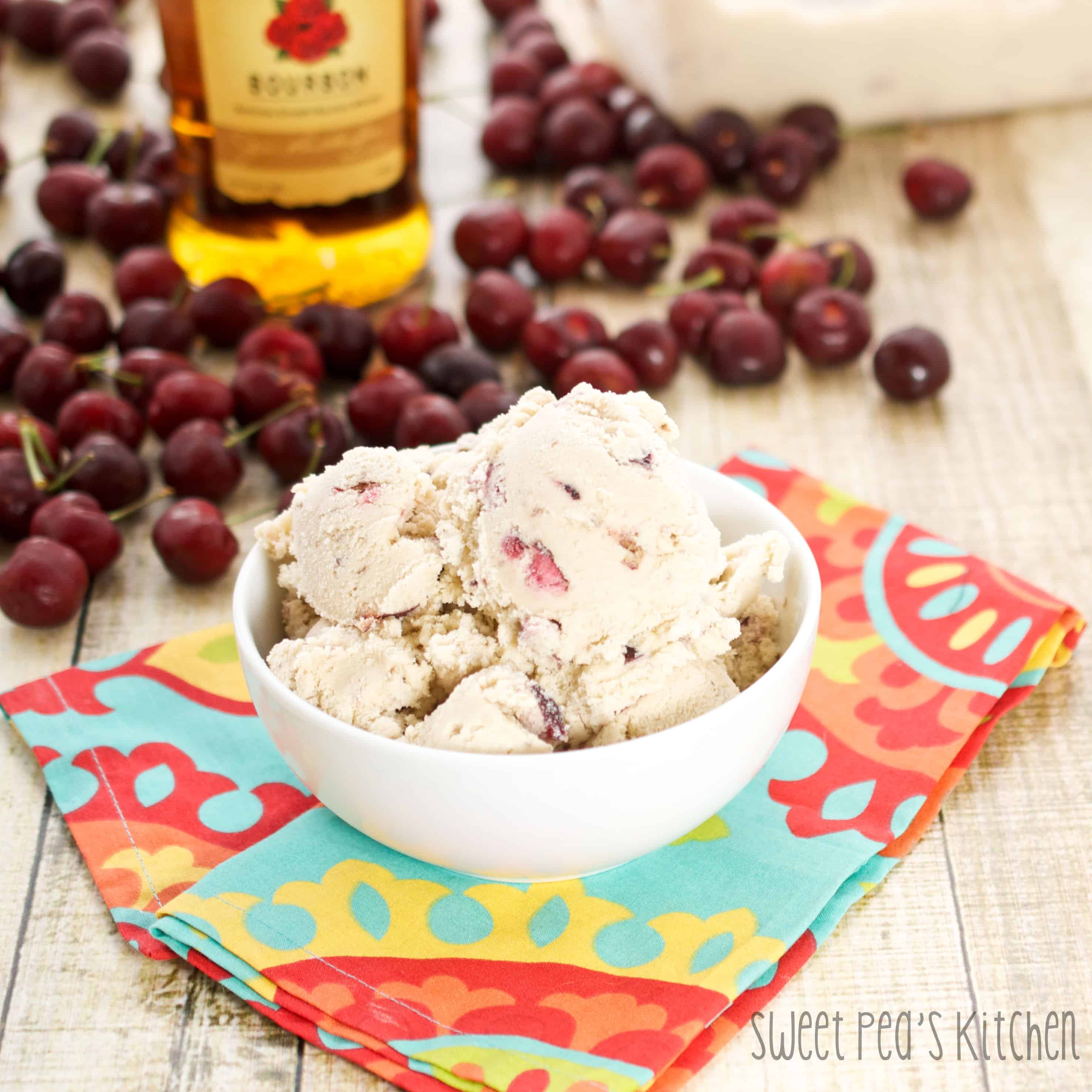A bowl of cherry ice cream with bourbon accents sitting on a wooden table with vibrant colored napkin under bowl