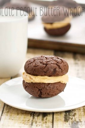 A single whoopie pie sitting on a saucer with a cup of milk behind it