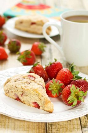 fresh strawberry scones recipe with a piece sitting on a white plate with fresh strawberries and coffee in the background