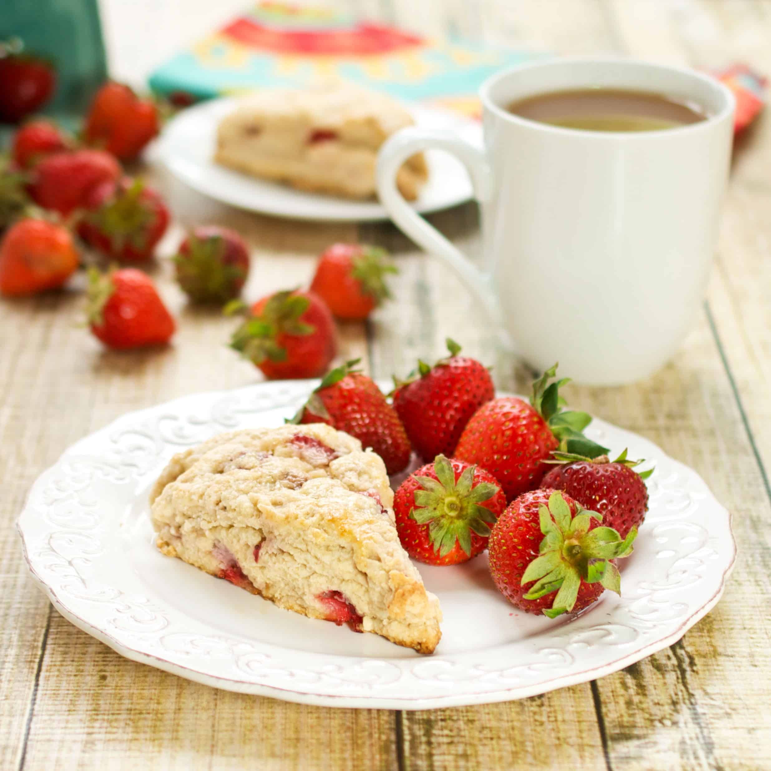 fresh strawberry scones recipe with a piece sitting on a white plate with fresh strawberries and coffee in the background