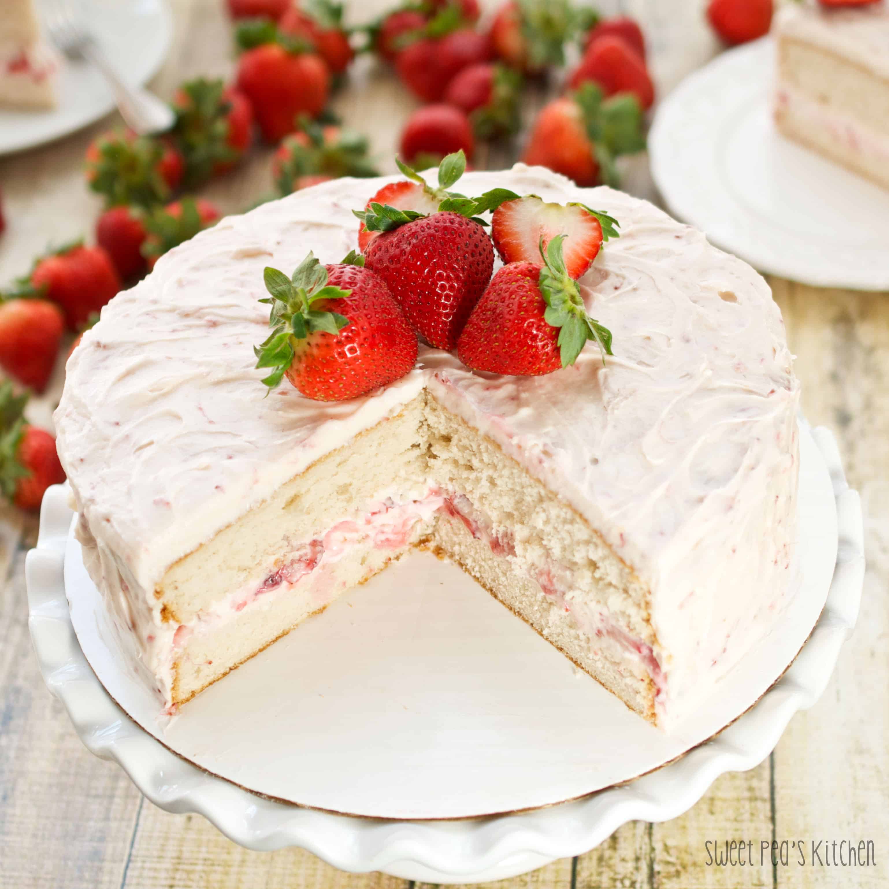 Strawberry cake on a white cake plate with a slice missing
