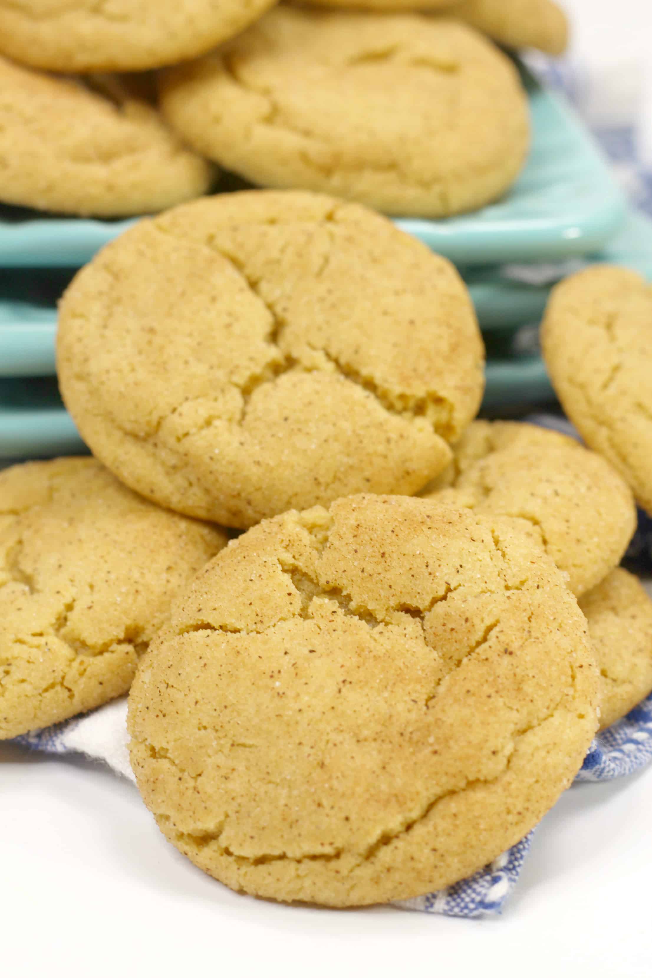 Stacks of Easy snickerdoodle cookies laying on a white surface next to teal plates