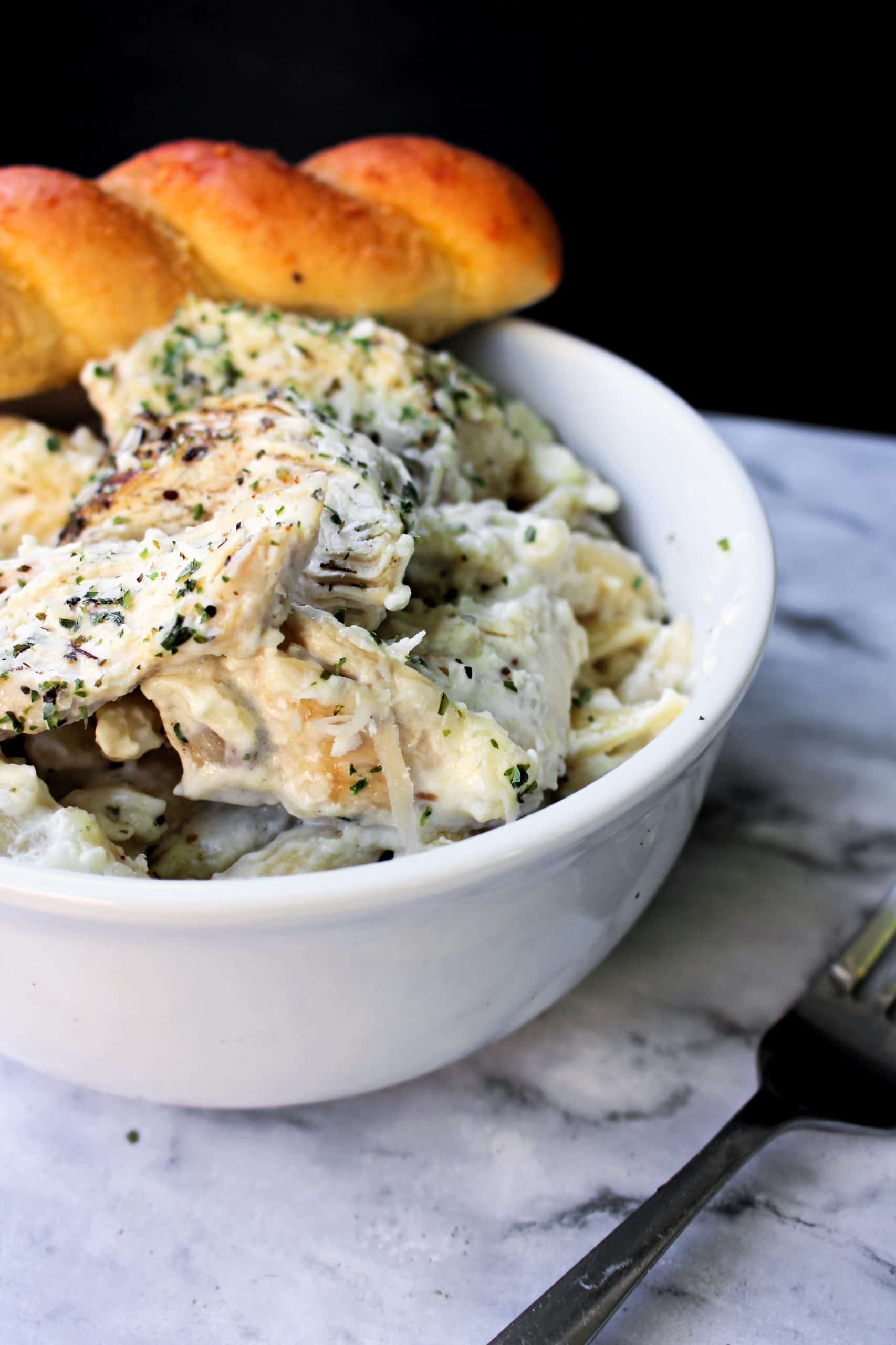 crockpot chicken alfredo in a white bowl with breadstick