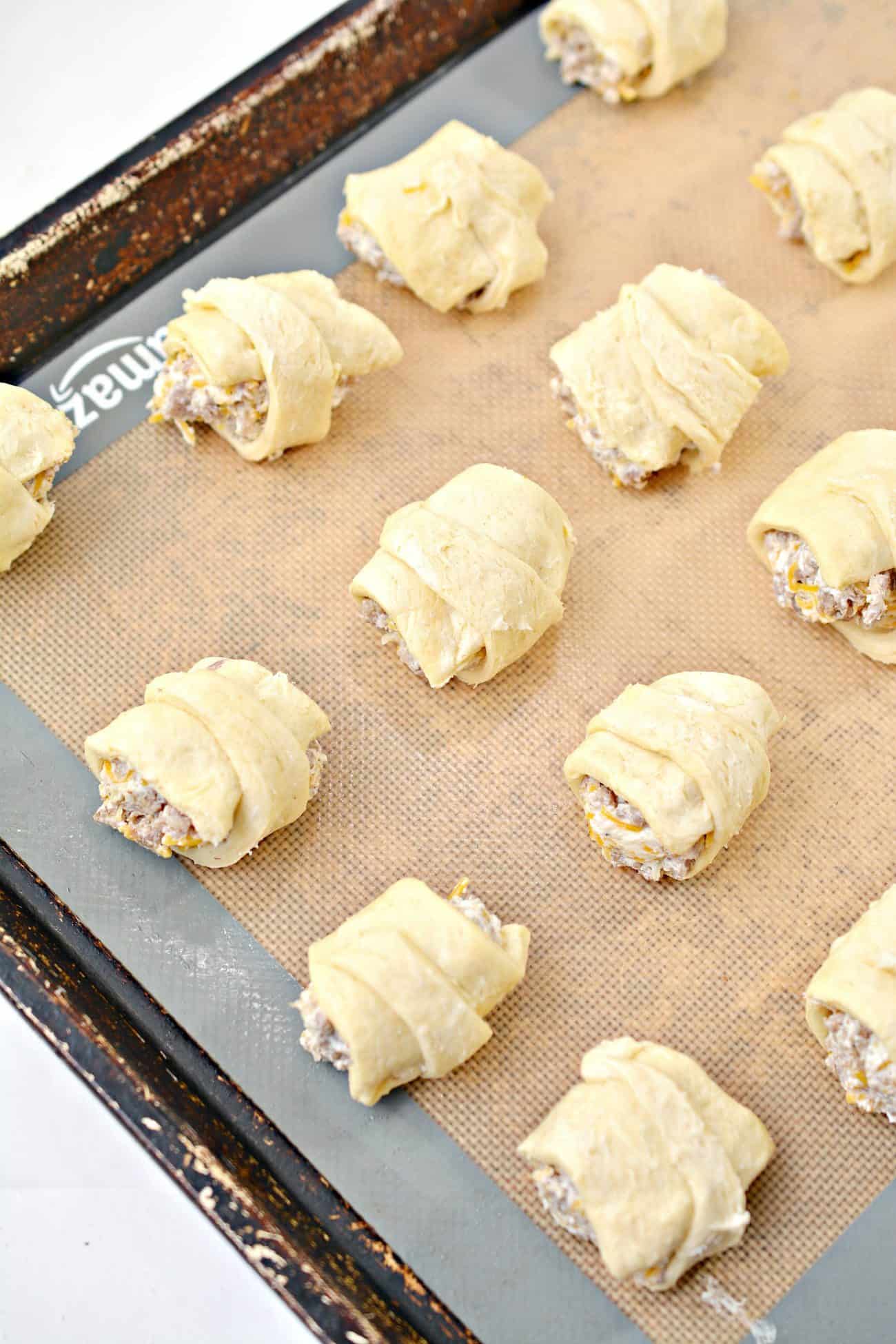 Starting at the widest end, roll the crescent roll dough over the sausage filling forming a mini stuffed crescent roll.