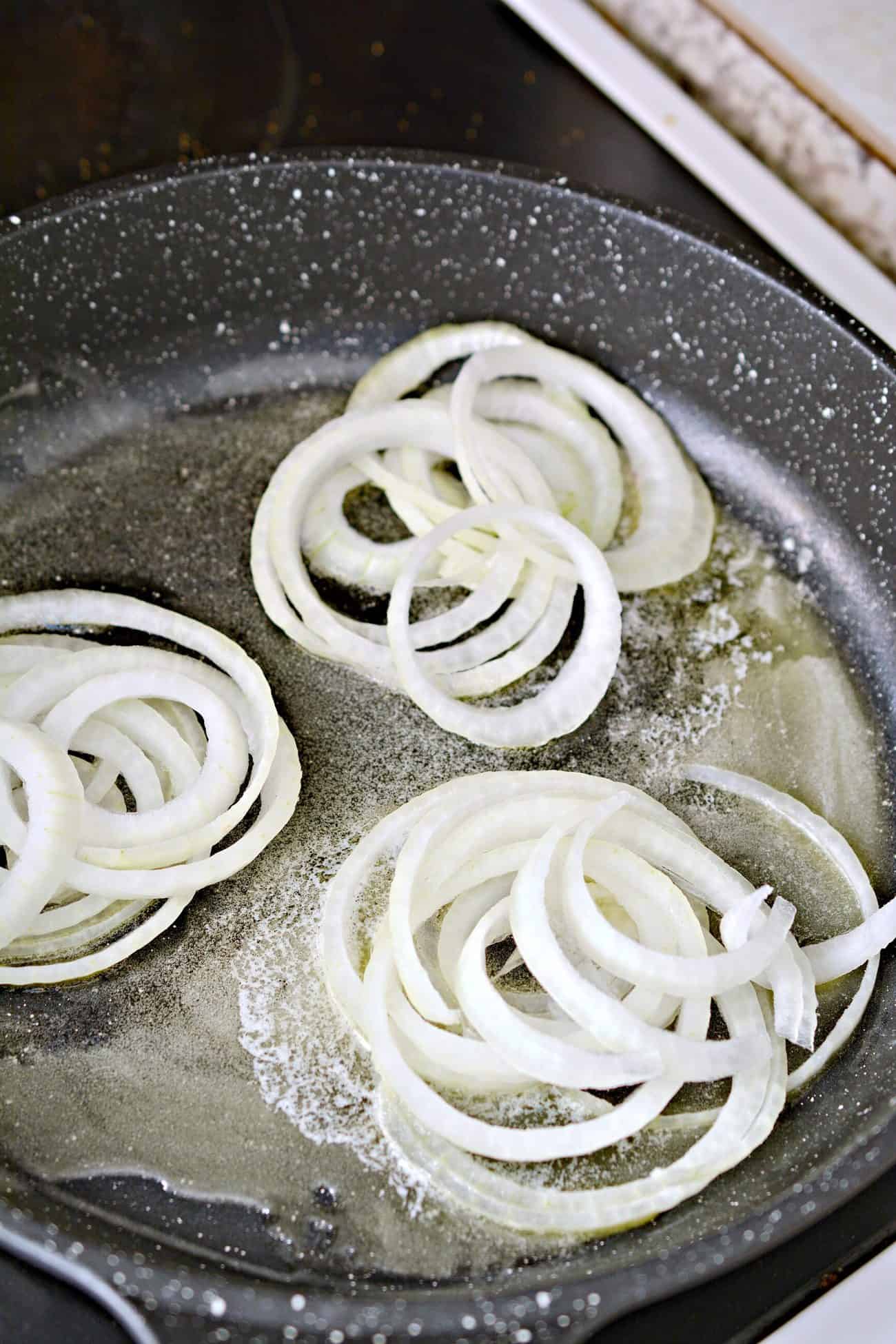 Add 2 tbsp of butter to a skillet over medium heat and place 5 piles of sliced onion into the skillet.