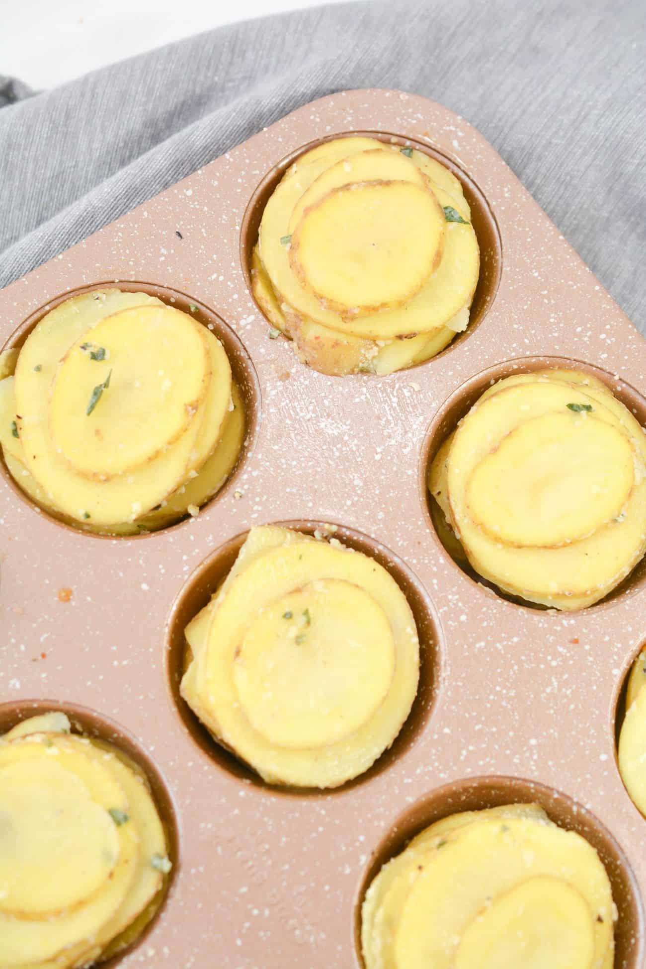 Stack the sliced potatoes up, and place them into the sections of a well-greased muffin tin