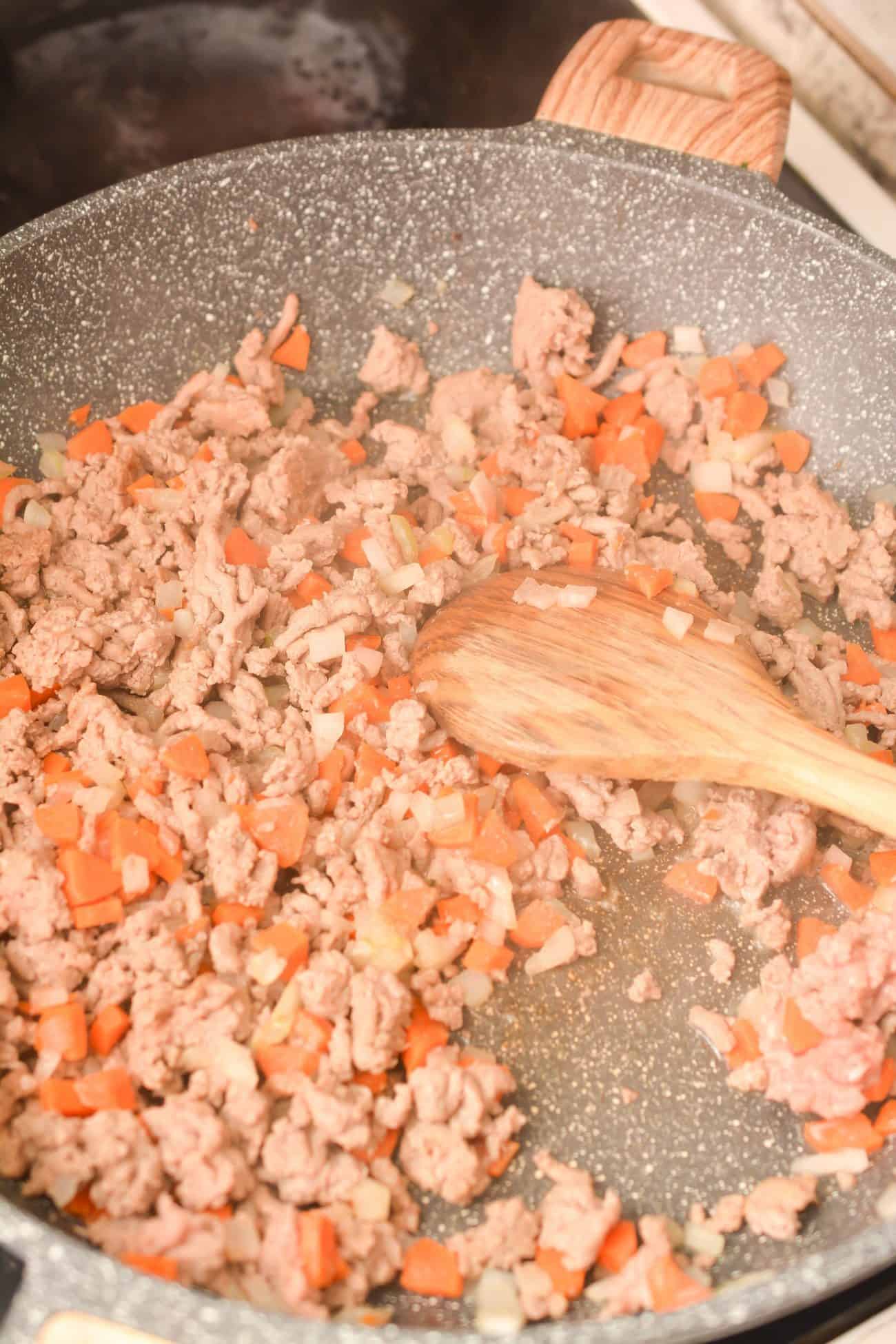 Place the ground pork, onions, and carrots in a skillet over medium-high heat and saute until the meat is completely browned and the vegetables have softened.