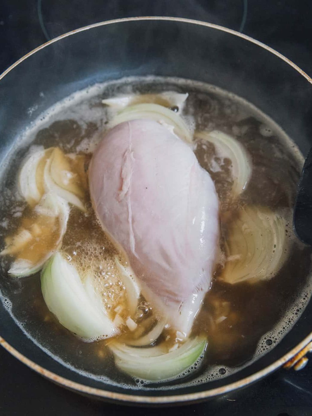 Place a pot on the stove over medium-high heat and pour in the chicken broth, and minced garlic, onion and place the chicken breasts. 