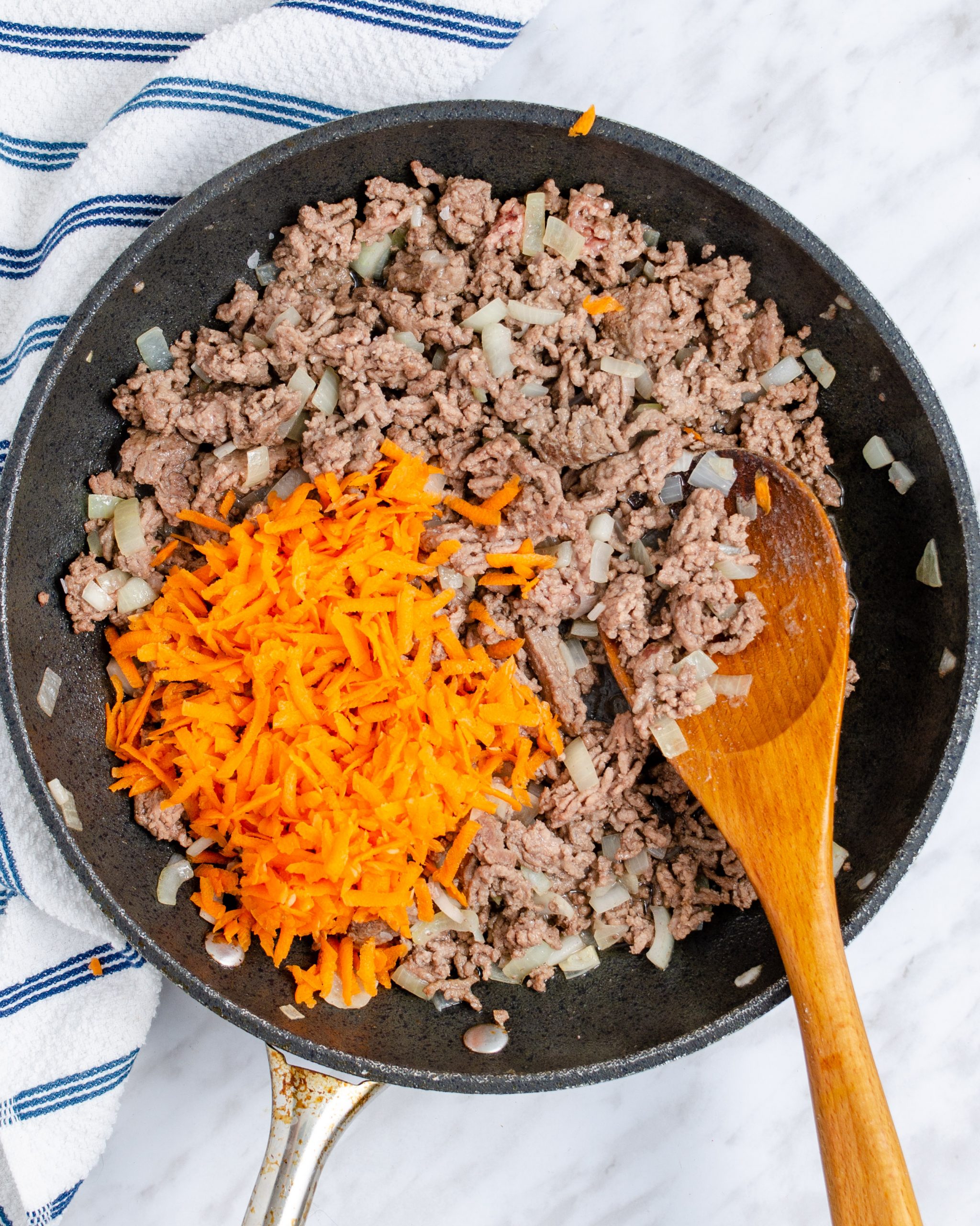 When the meat is halfway browned, mix the shredded carrots into the skillet.