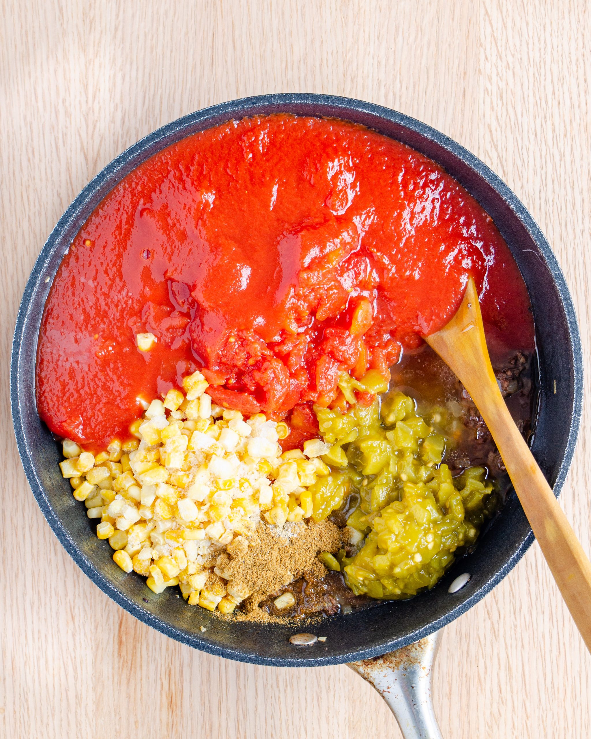 Reduce the heat to medium and add in the diced tomatoes, frozen corn, tomato sauce, green chilis, salt and pepper, and cumin. Stir to combine.
