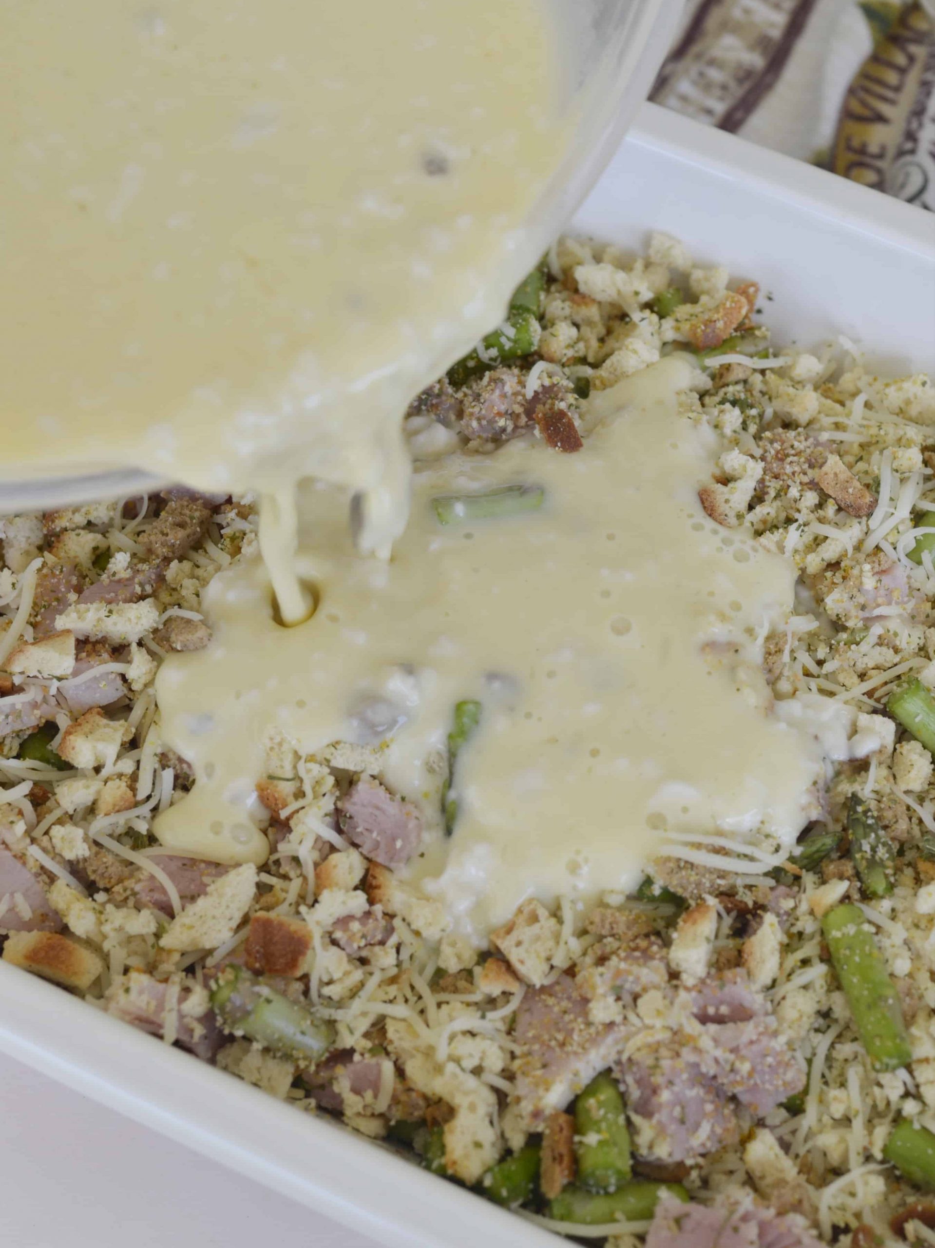 stuffing casserole with ham pouring filling over the top