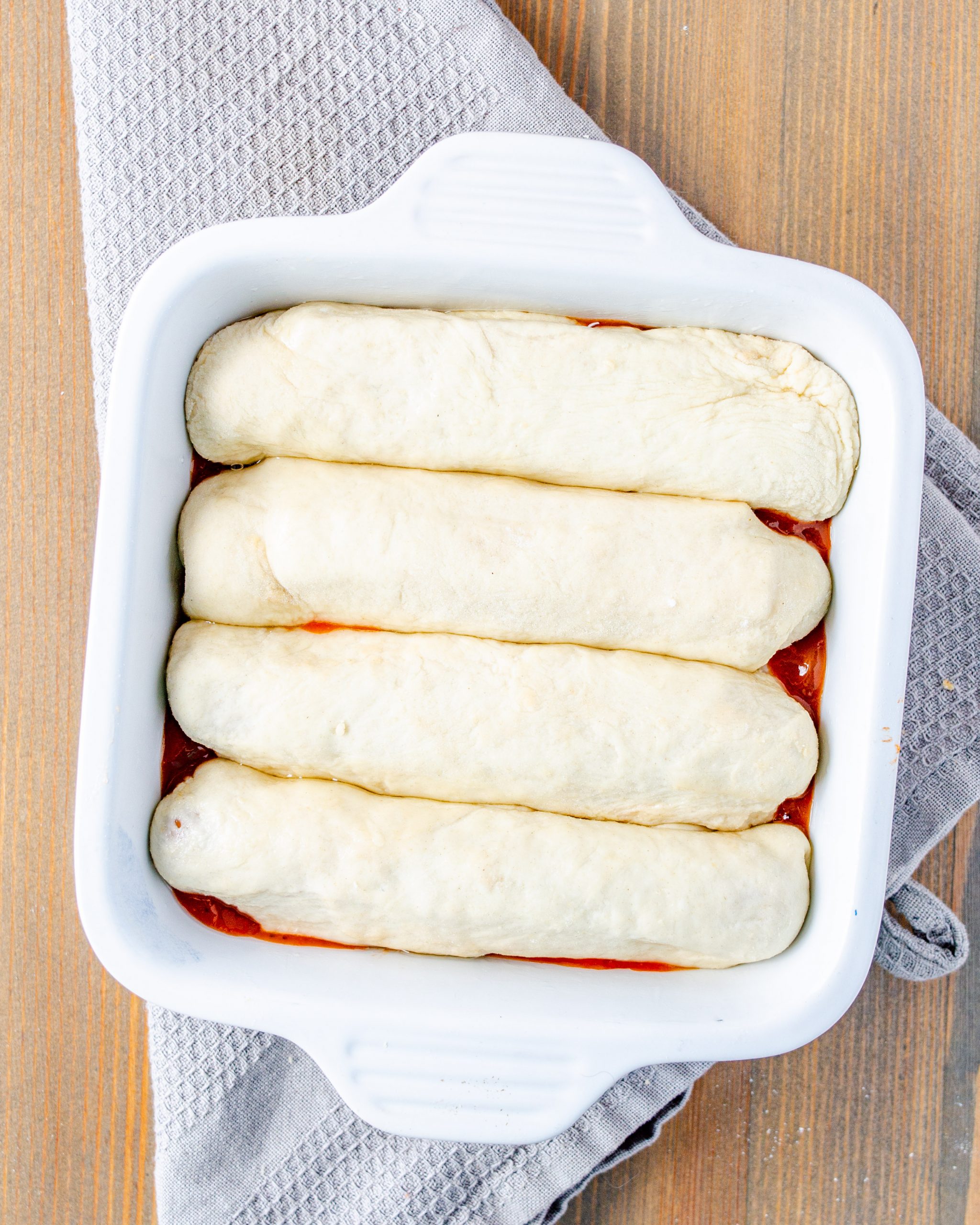 Place the wrapped hot dogs into the baking dish on top of the hot chili sauce and bake for 20-25 minutes until cooked through and golden brown on top.