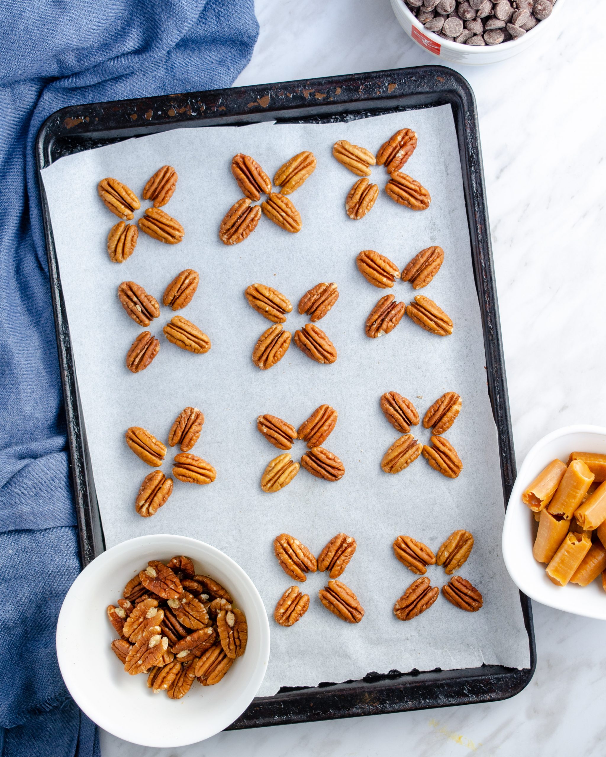 Place the pecan halves flat side down on a parchment or silicone baking mat-lined baking sheet. Separate them into sets of four, and form them into cross or “x” shapes. Leave some room between each set of four pecan halves. These will be the base for your turtle candies.