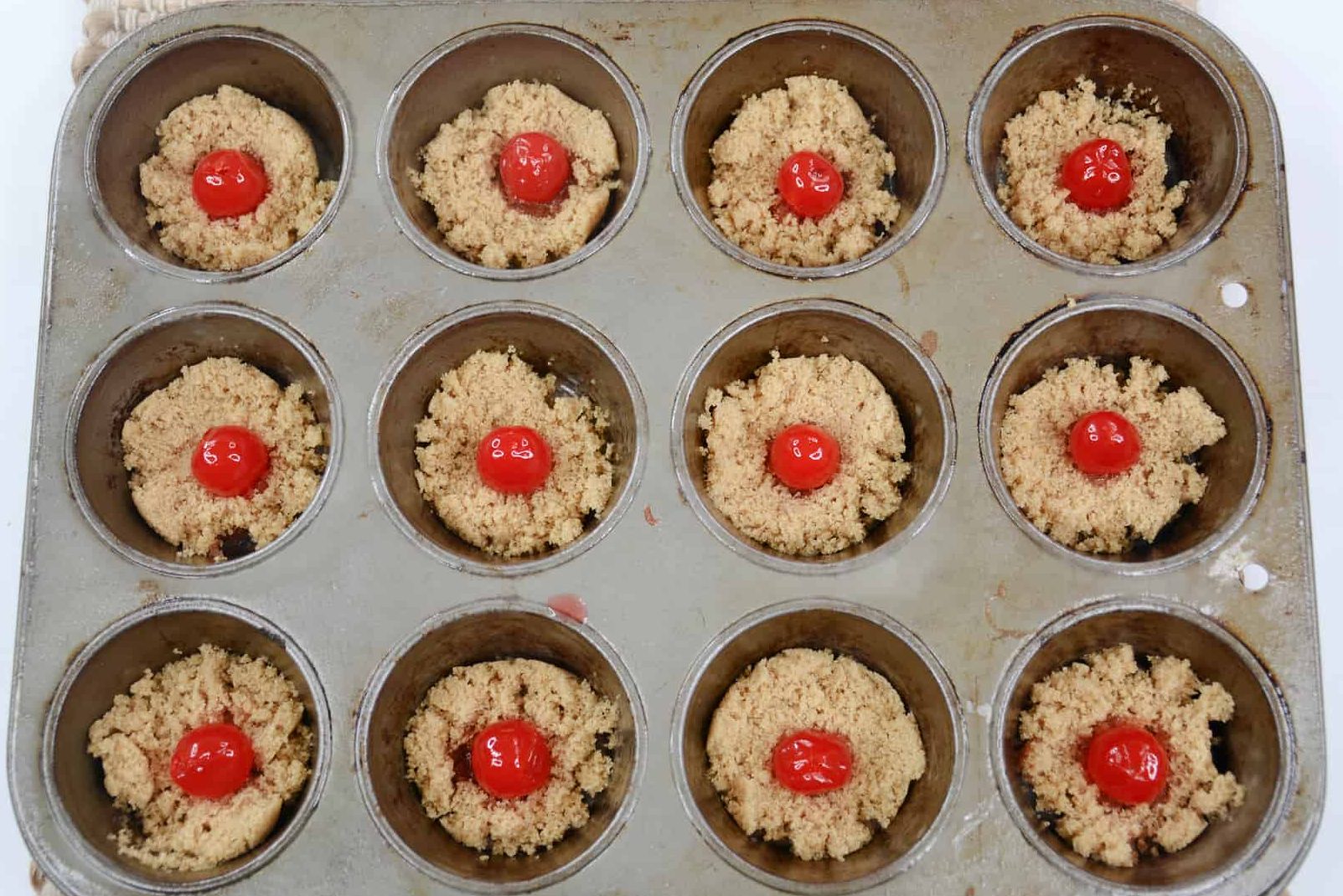 Position one maraschino cherry in the center of the light brown sugar in each of the muffin cups.