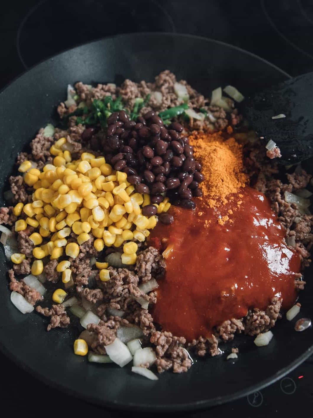 Add the taco seasoning, green chilli, black beans, frozen corn and enchilada sauce to the skillet with the meat.