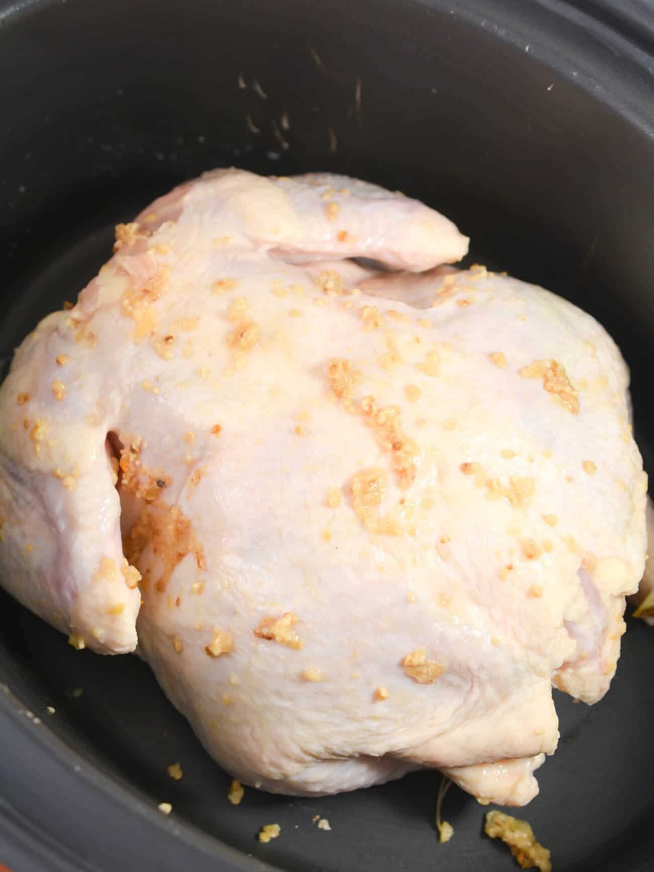 Rub half of the minced garlic on the inside of the chicken, and the other half on the outside. Place the chicken into the Crockpot.