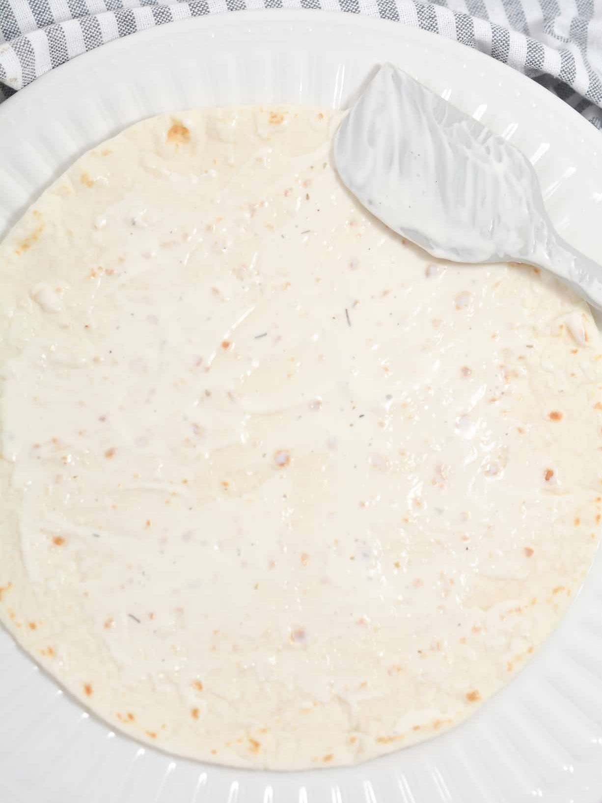 Spread some ranch dressing on one side of two different tortillas, and lay them on a counter dressing side up.