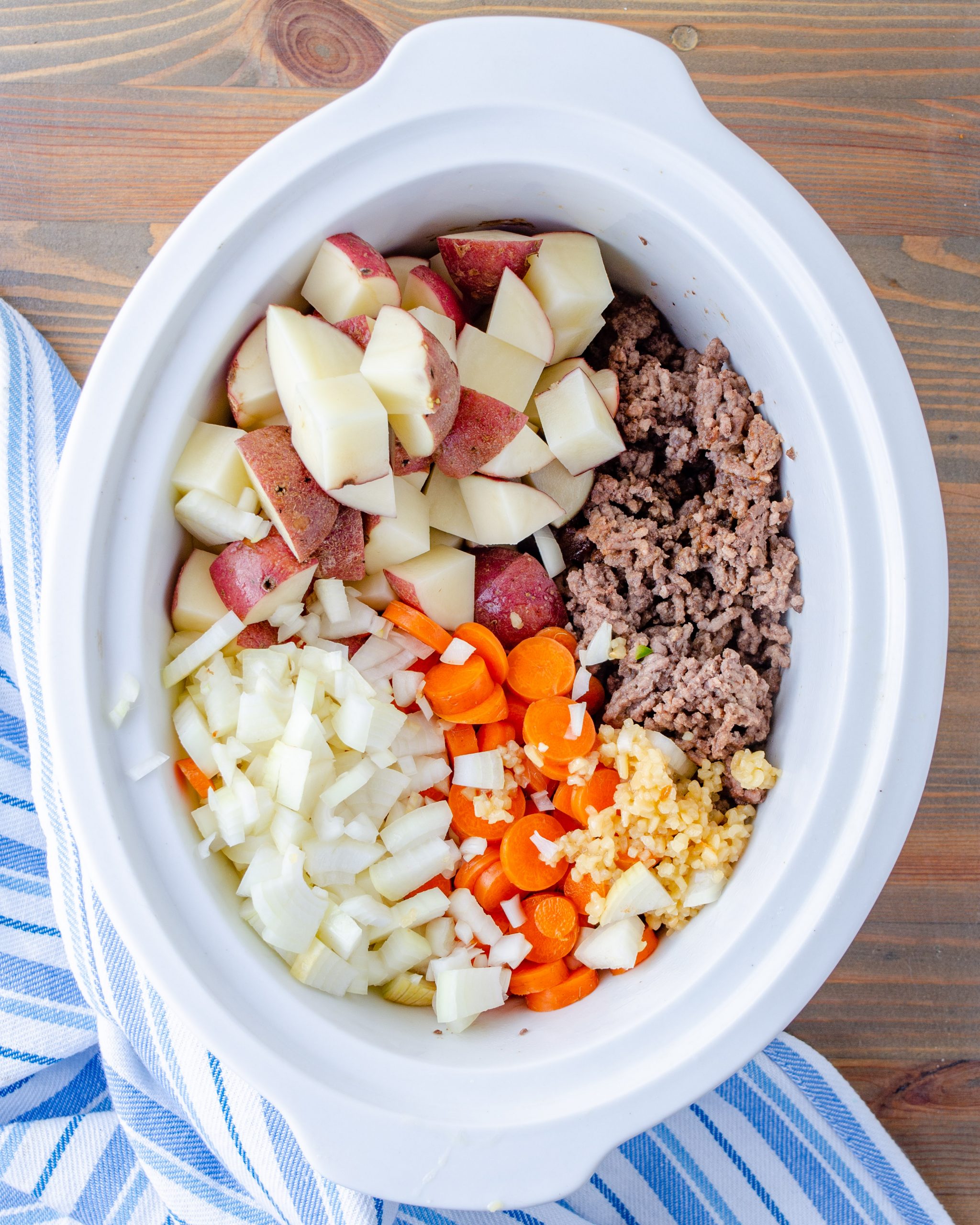 Place the ground beef into the slow cooker along with the potatoes, onions, and carrots. Stir to combine.
