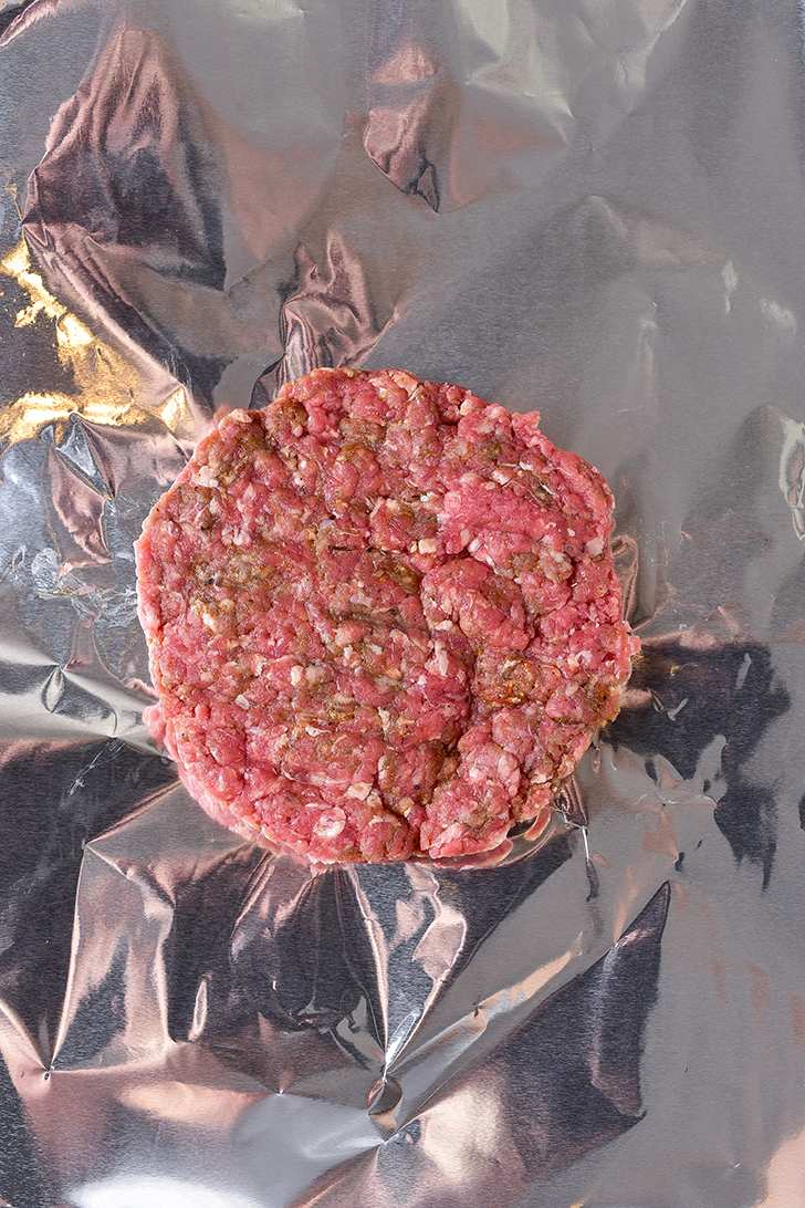 Place one meat patty into the center of each of four large squares of tin foil. 