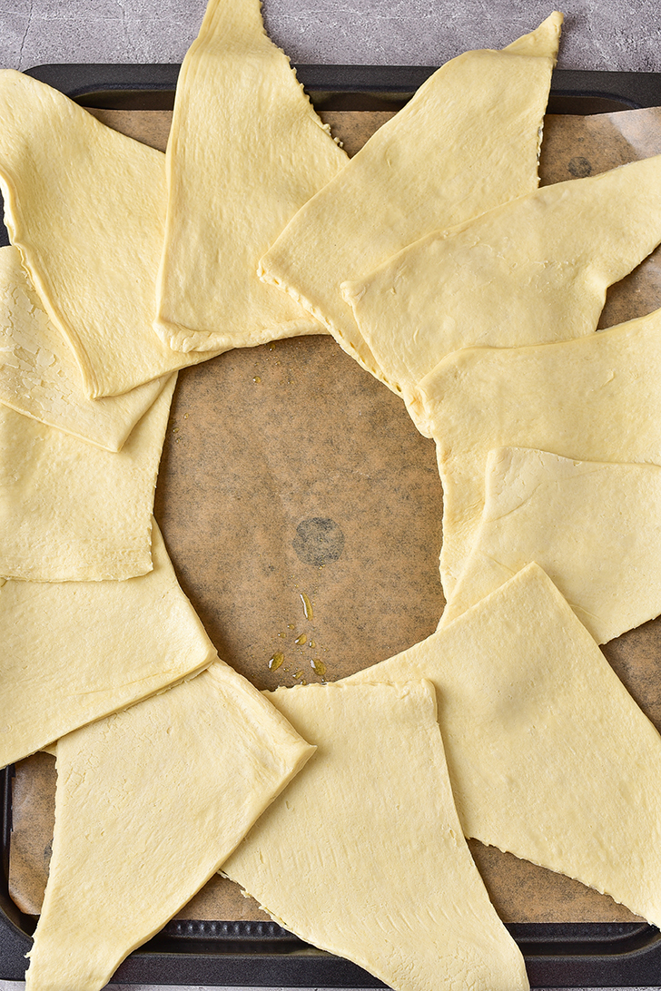 Place the dough triangles in a circular shape on the round baking sheet, with the wide ends of the dough all overlapping and creating the inner part of the circle, and the pointy ends of the dough facing outward like the shape of a sun.