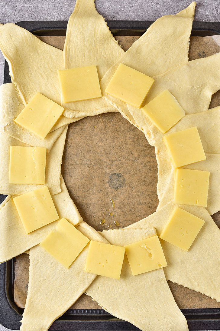Lay the half slices of provolone cheese on the widest part of the dough triangles, near the center of the ring.