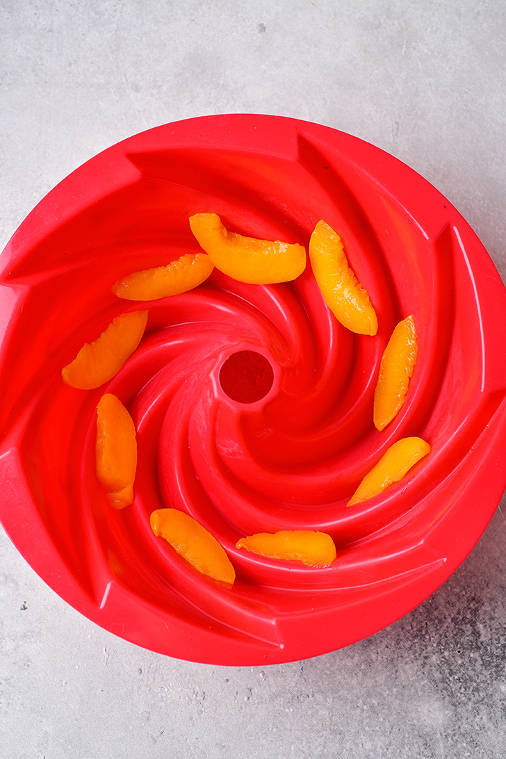 Place a layer of the sliced peaches into the bottom of a well-greased bundt pan. 
