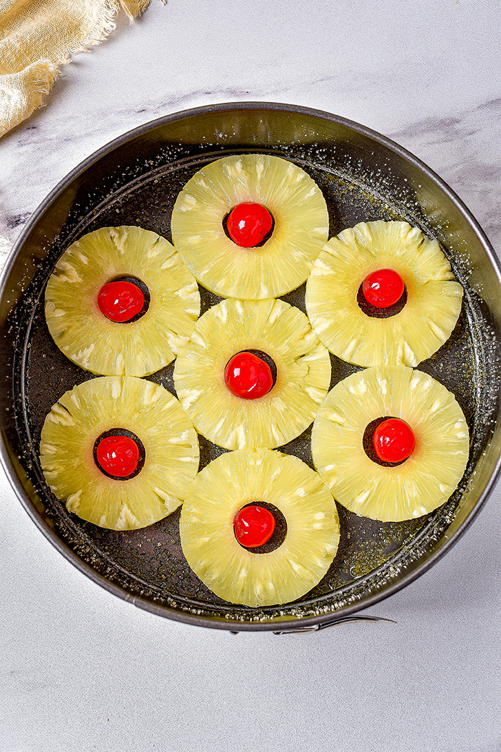 Top the butter mixture with the slices of pineapple, and place a cherry in the center of each pineapple slice. 