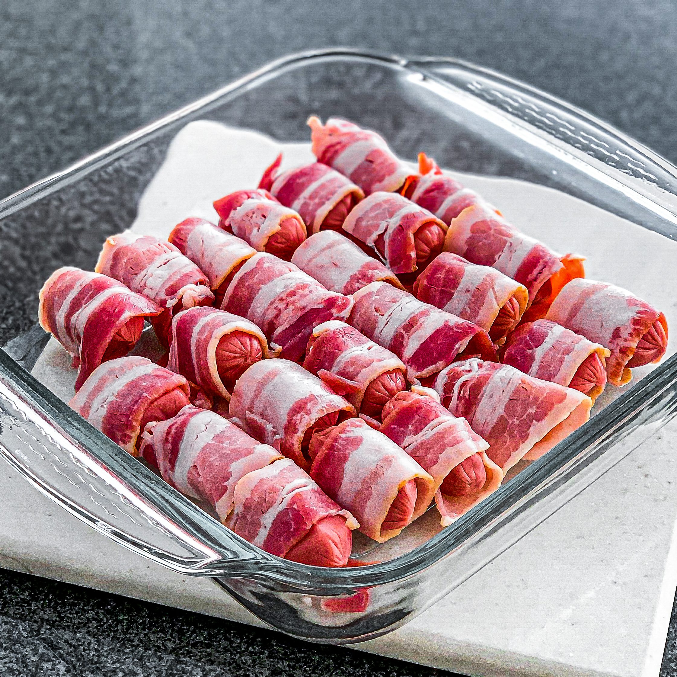 Arrange each one of the bacon-wrapped sausages into a baking dish.