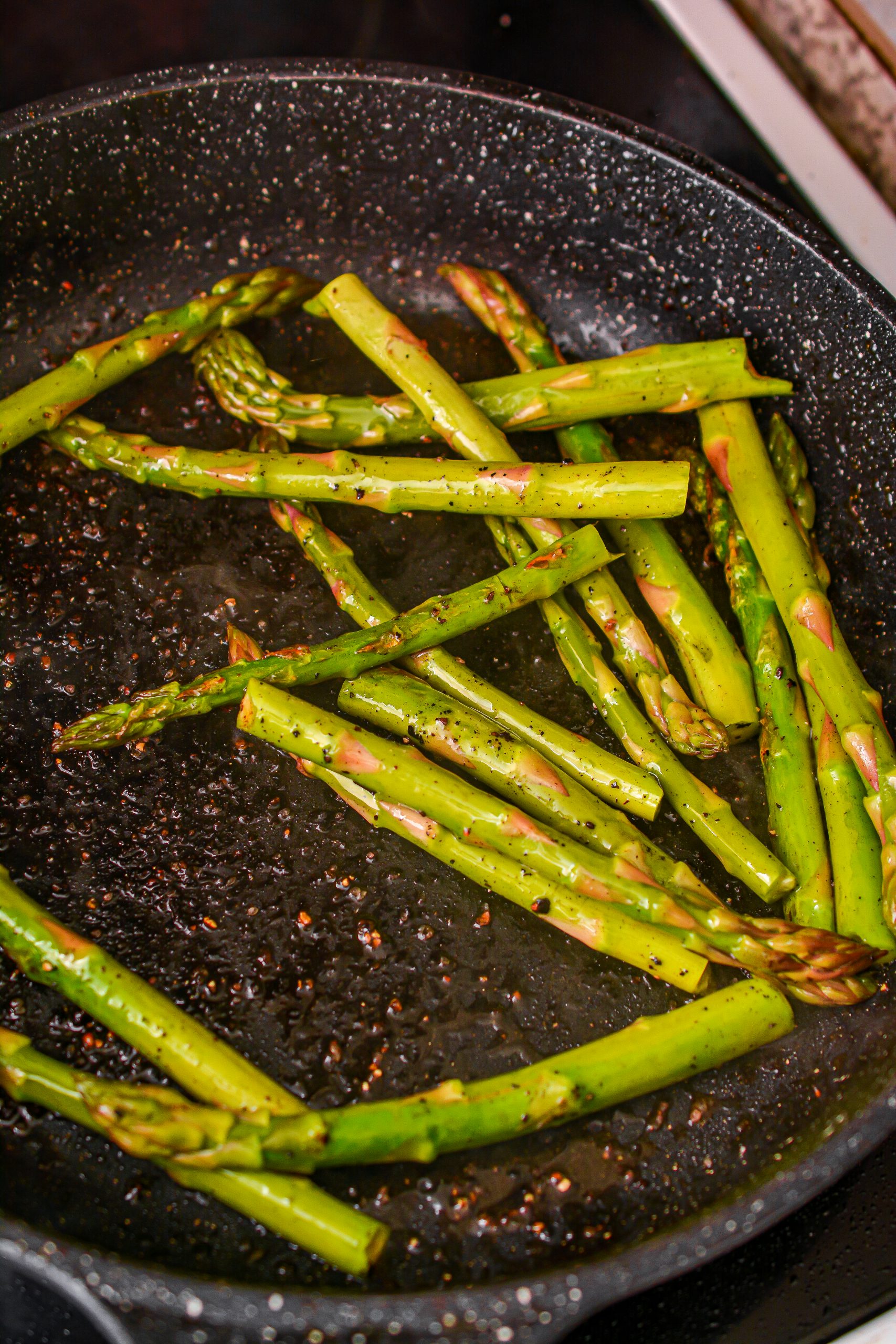 Place the asparagus in the skillet, turn the heat down to medium, place the lid on, and cook until becoming tender. Season with salt, pepper, and oregano