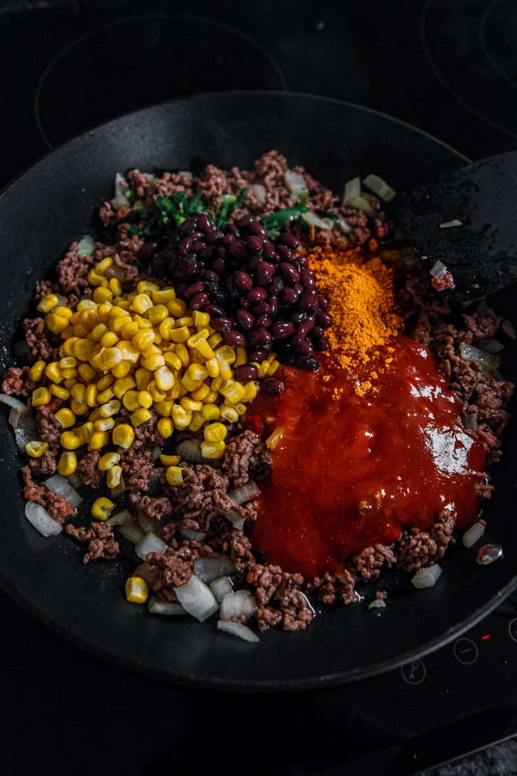 Add the taco seasoning, green chilli, black beans, frozen corn and enchilada sauce to the skillet with the meat.