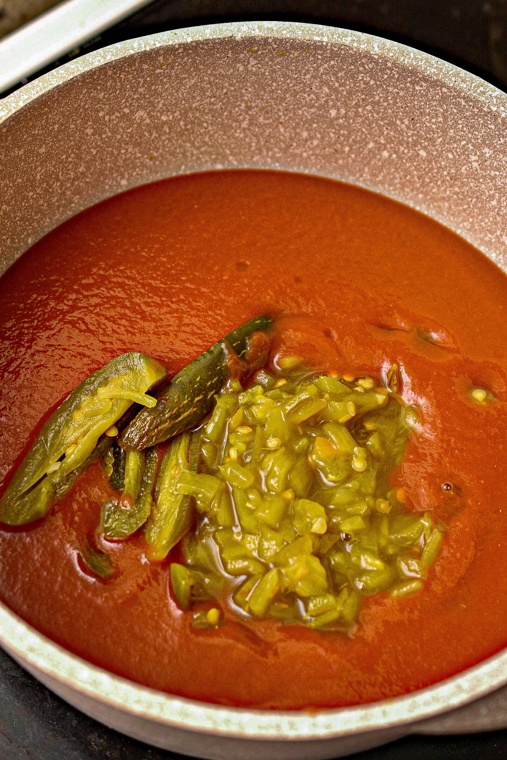 Pour the rest of the tomato sauce, the green chilis, and the jalapeno peppers into a saucepan over medium heat on the stove
