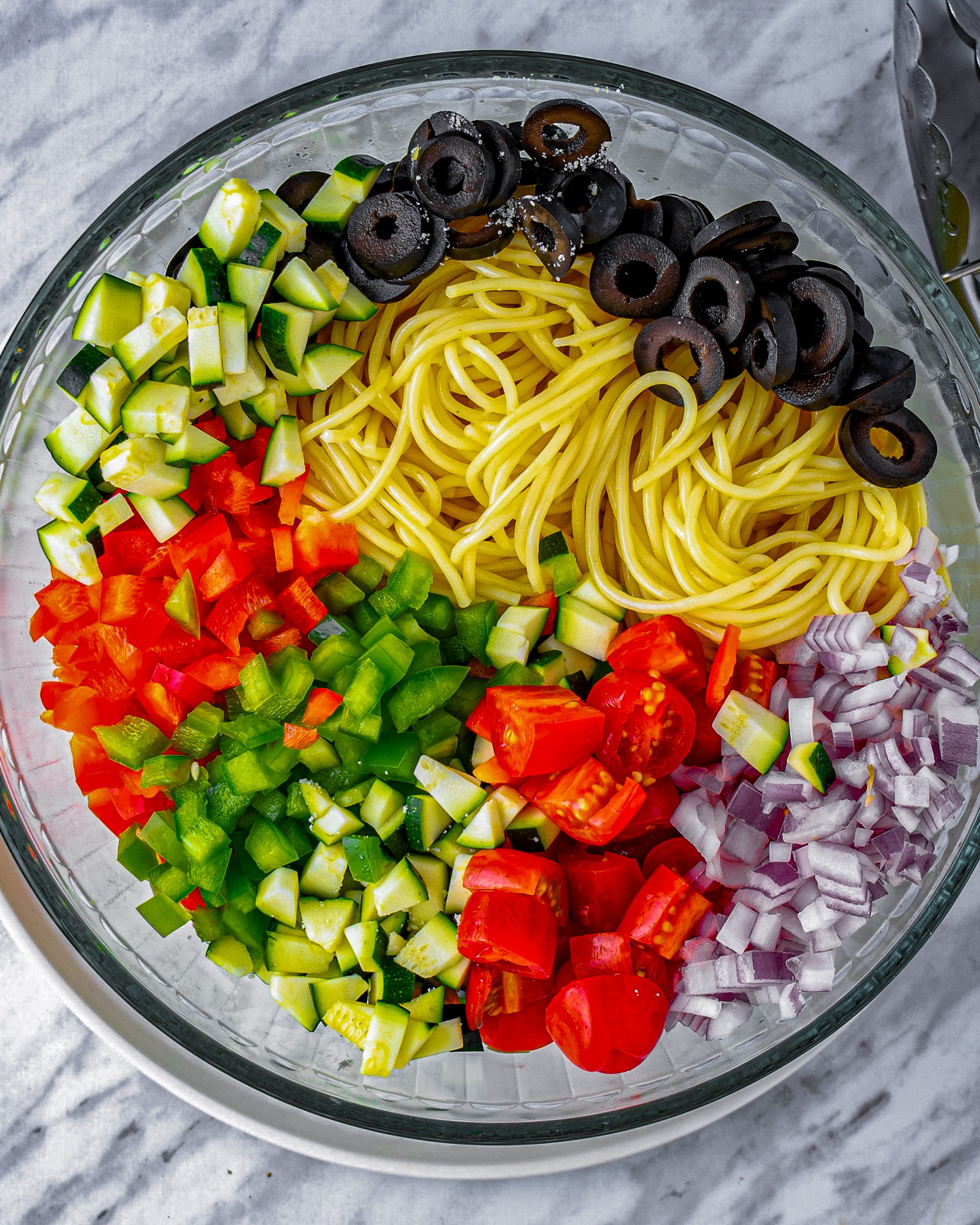 In a large mixing bowl, combine the spaghetti, red bell pepper, green bell pepper, cucumber, zucchini, tomatoes, red onion, and black olives.