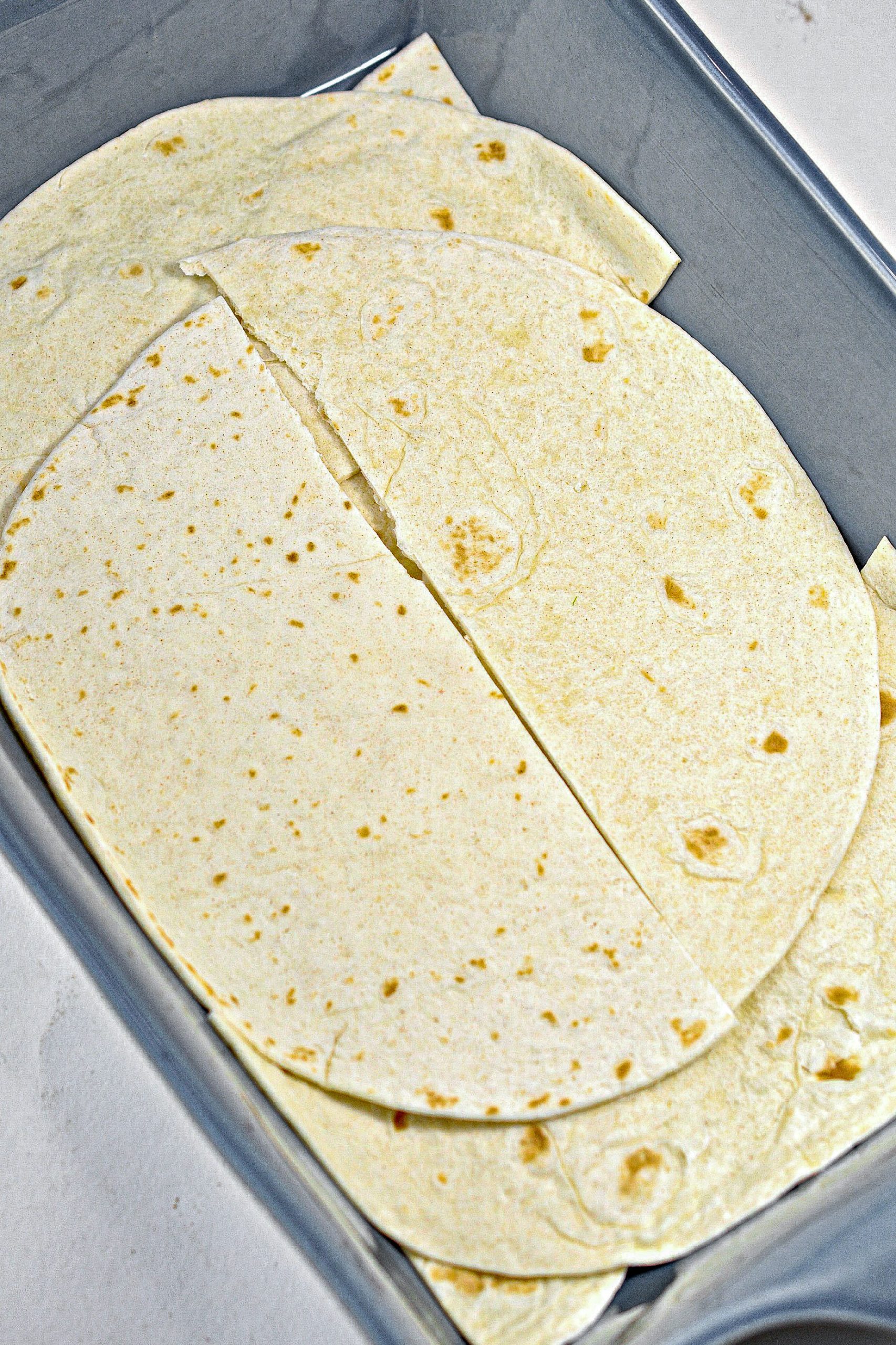 Place a layer made of 4 of the flour tortillas that have been cut in half in the bottom of a well-greased 9x13 baking dish.