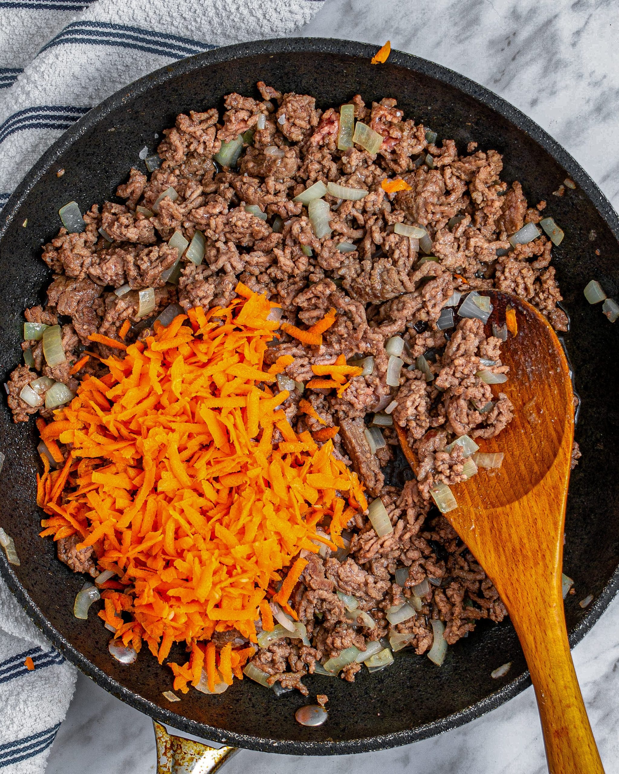 When the meat is halfway browned, mix the shredded carrots into the skillet.