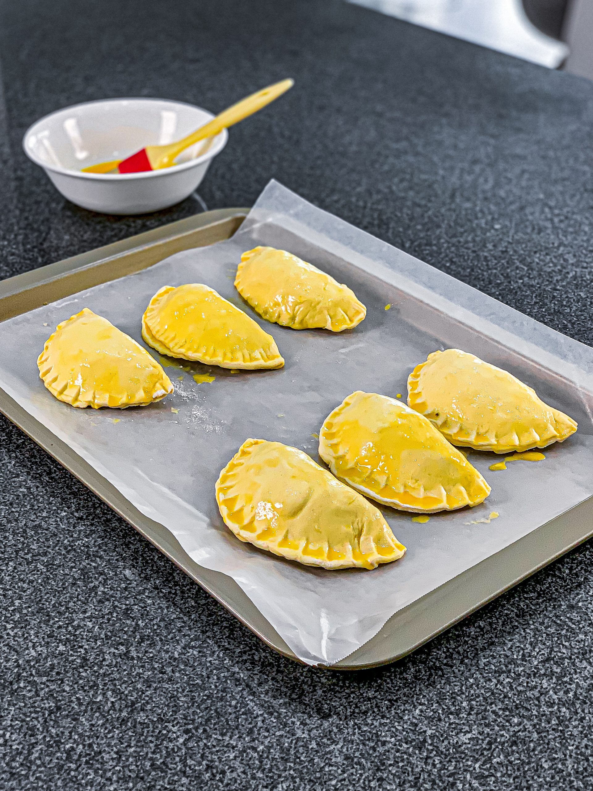 Transfer the meat pies to a lined baking sheet and brush the top of the dough with beaten egg.
