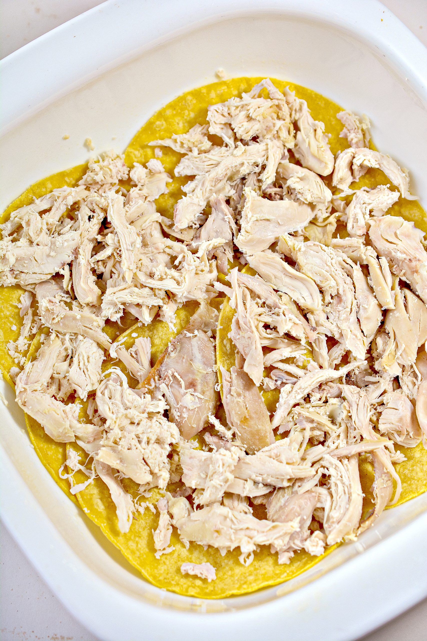 Place a layer of half of the shredded chicken on top of the tortillas in the baking dish.
