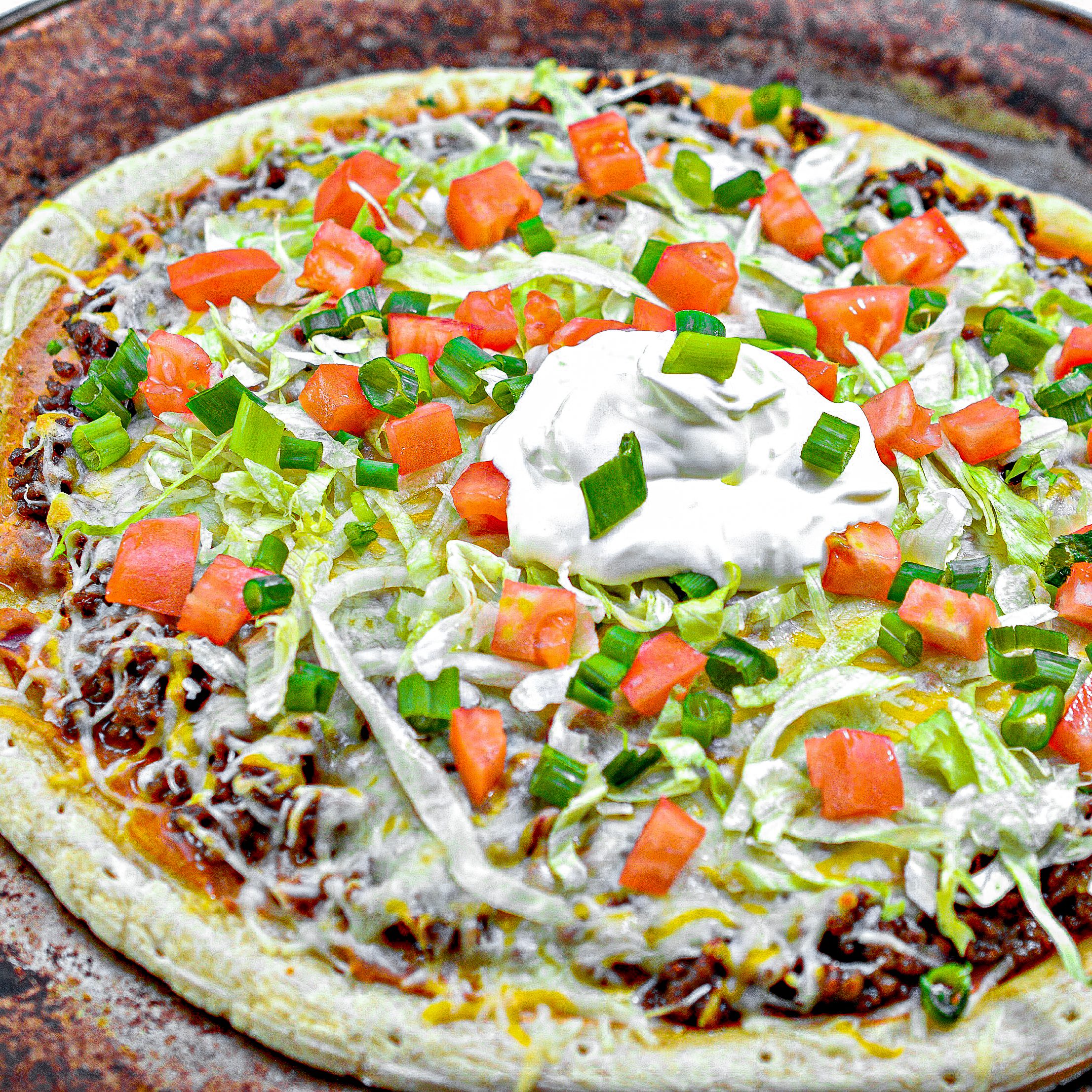 Top the pizza with the shredded lettuce, tomatoes, green onions, sour cream, and any other toppings you may desire before serving.