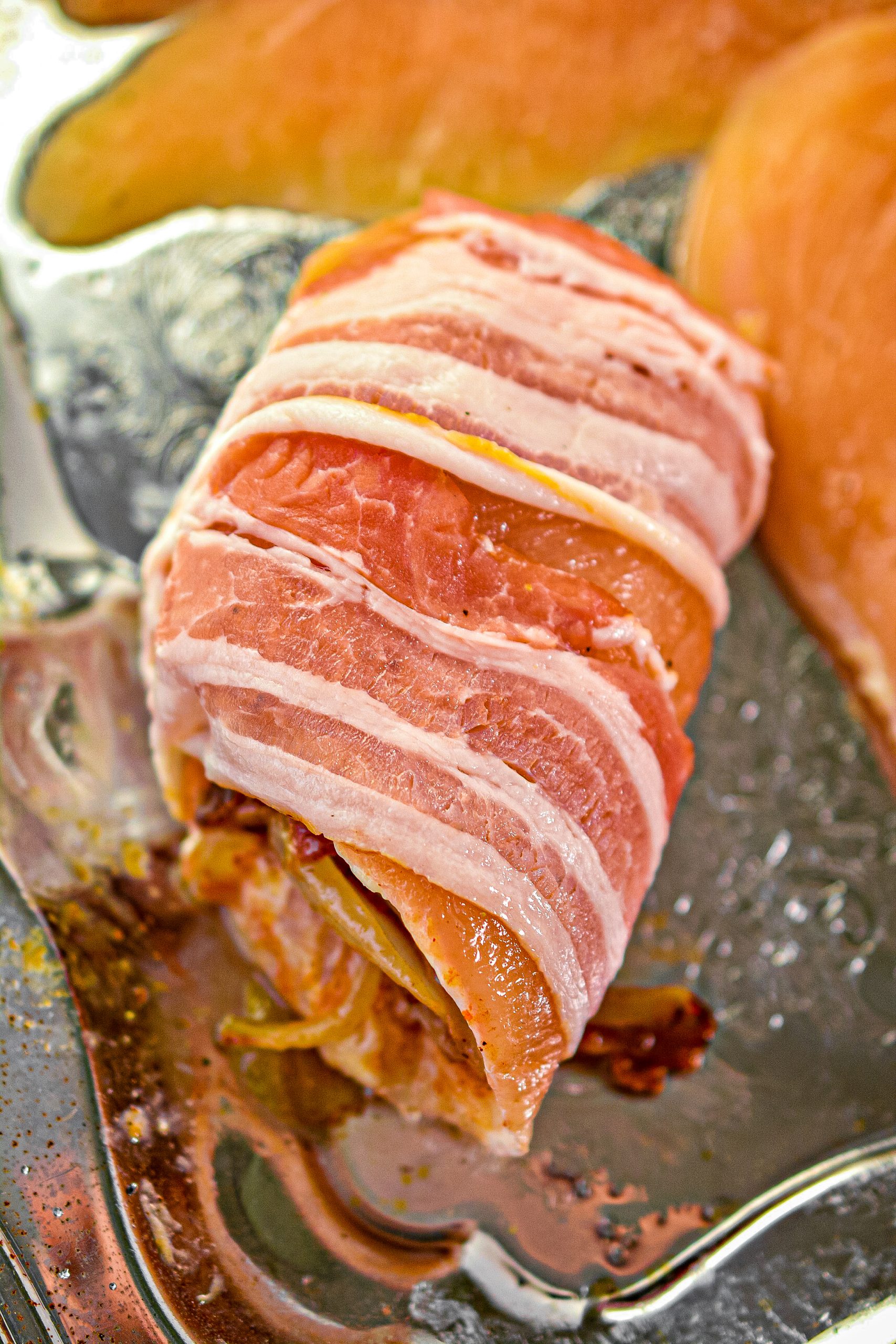 Wrap an uncooked piece of bacon around the outside of the rolled chicken breast, and place it on a baking sheet.