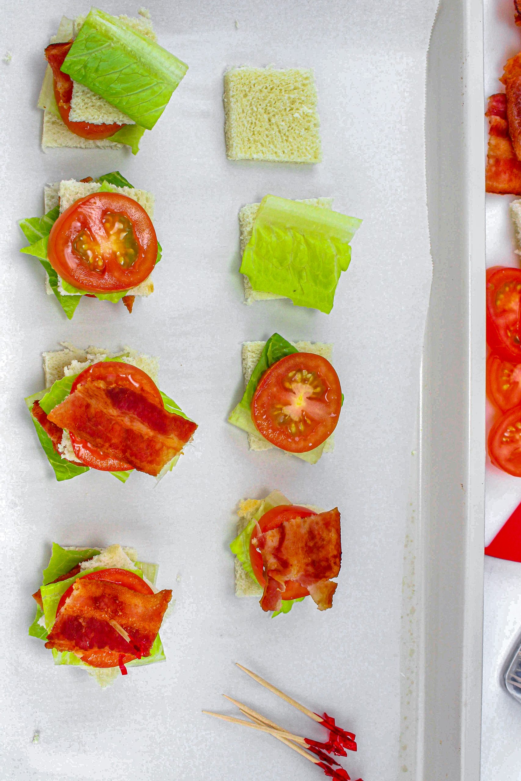 Lay out 16 squares of bread and set a piece of lettuce on them followed by a tomato slice and piece of bacon.