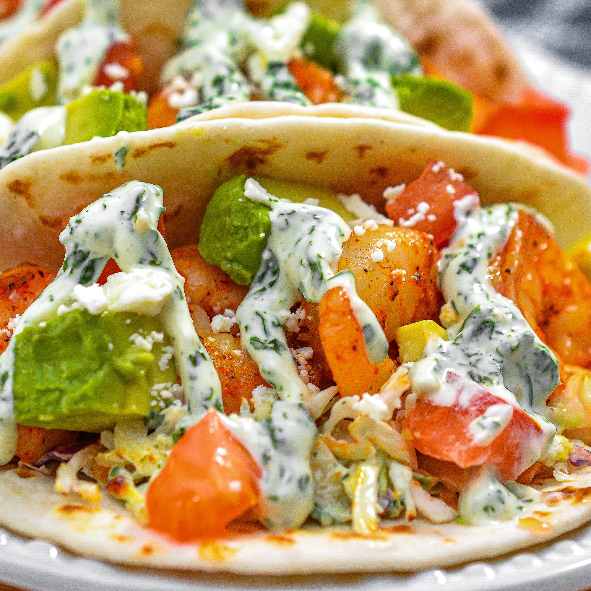 Place a layer of the coleslaw mixture in the bottom of the tortillas, top with shrimp and garnish with the tomatoes, feta cheese and avocado.