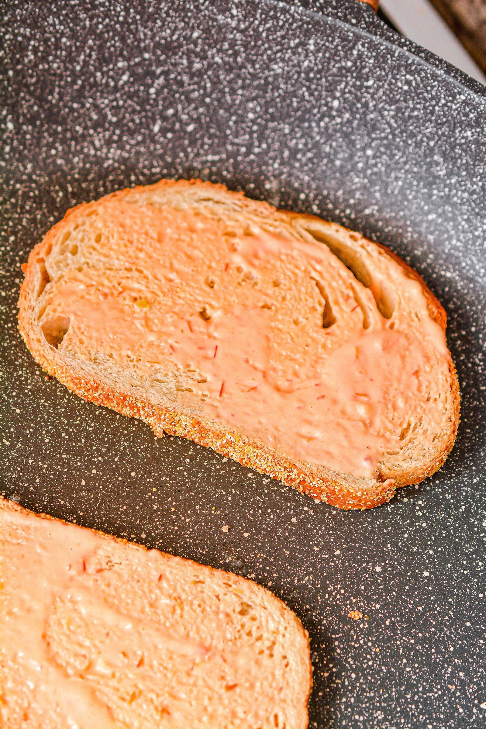 Add a layer of dressing to the other side of the slices of bread in the skillet.