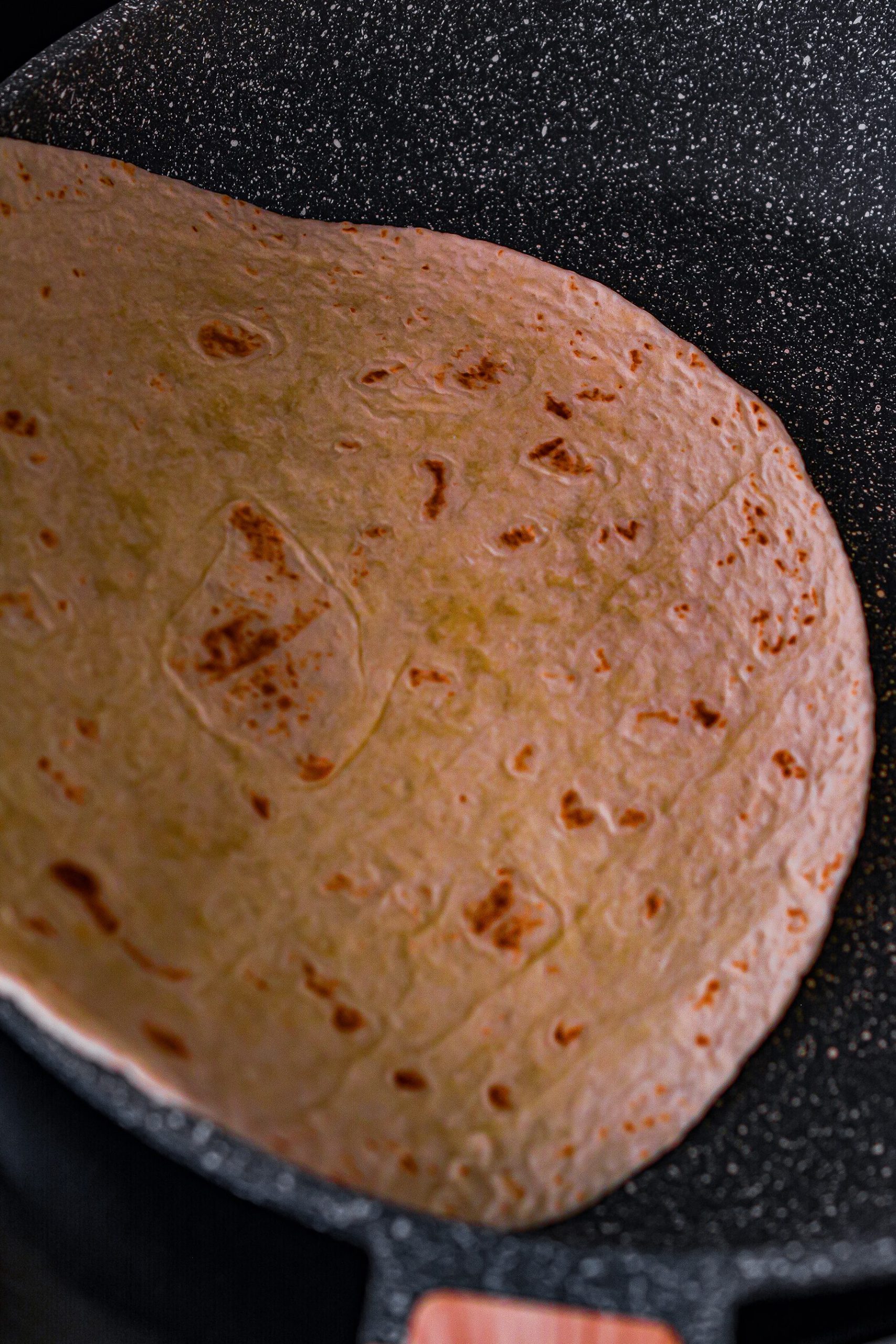 Spray some cooking oil into the large skillet and place a large flour tortilla in it.
